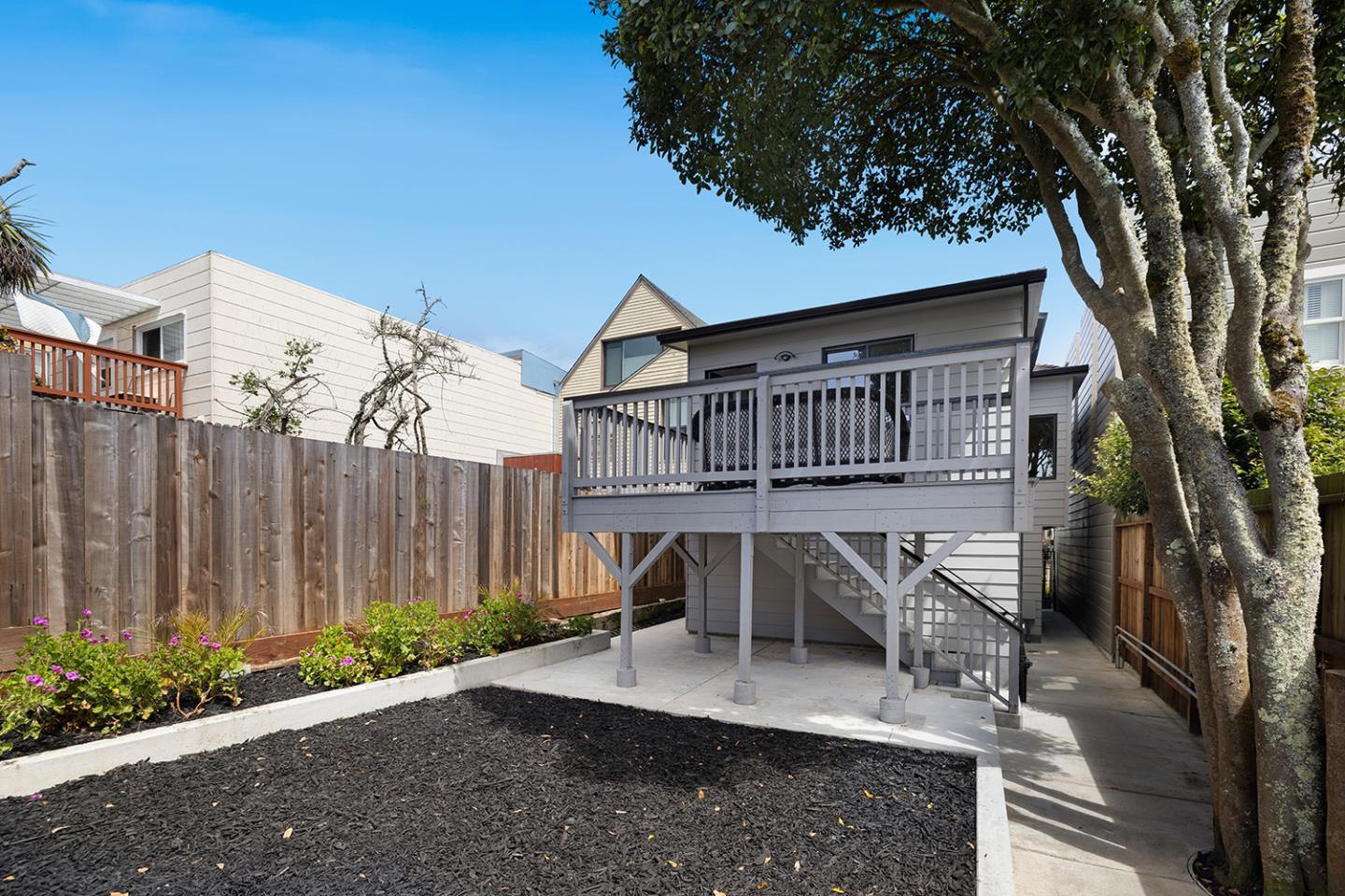 Home’s raised rear deck overlooks a fenced yard with garden beds and a large tree.