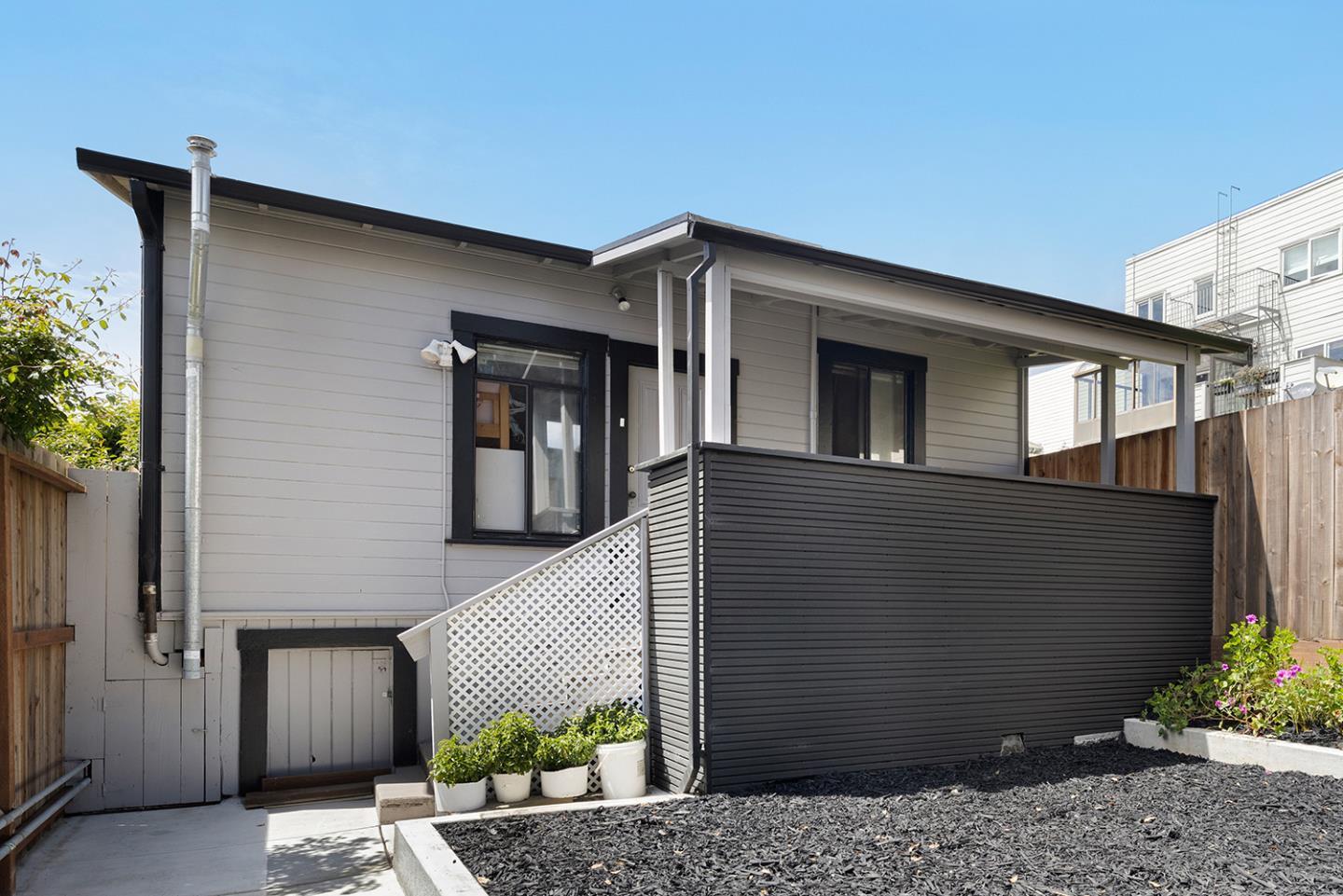 Rear exterior of a gray house with a covered deck, dark privacy screen, lattice stairs, and fenced yard.