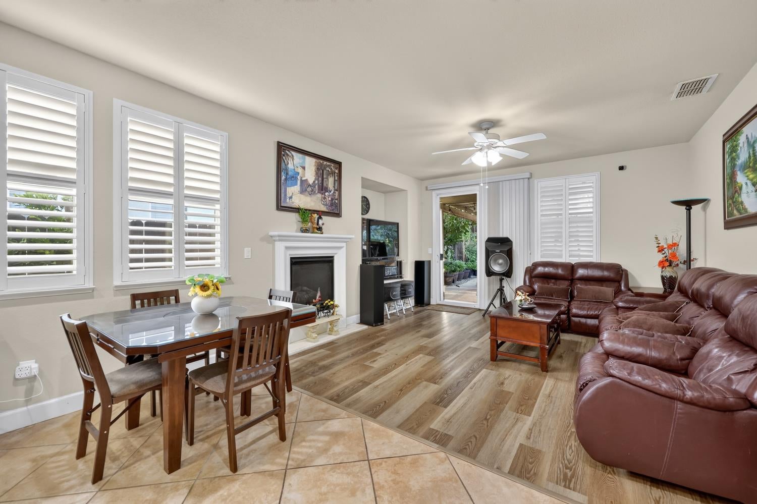 Open-plan living and dining room with a white fireplace, glass-top table, and brown leather sectional.