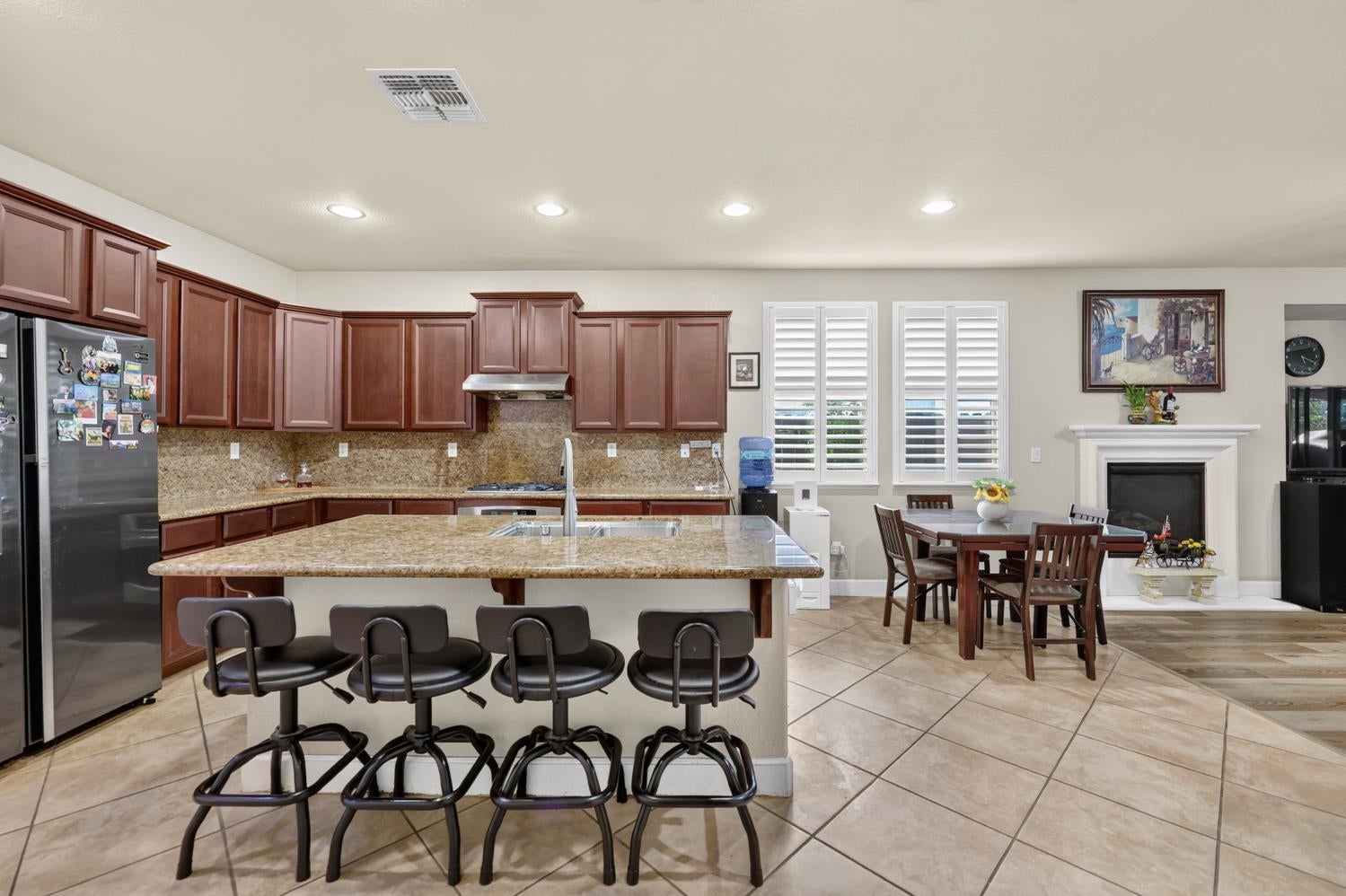Kitchen with a granite island and bar stools, adjoining a dining area and fireplace.