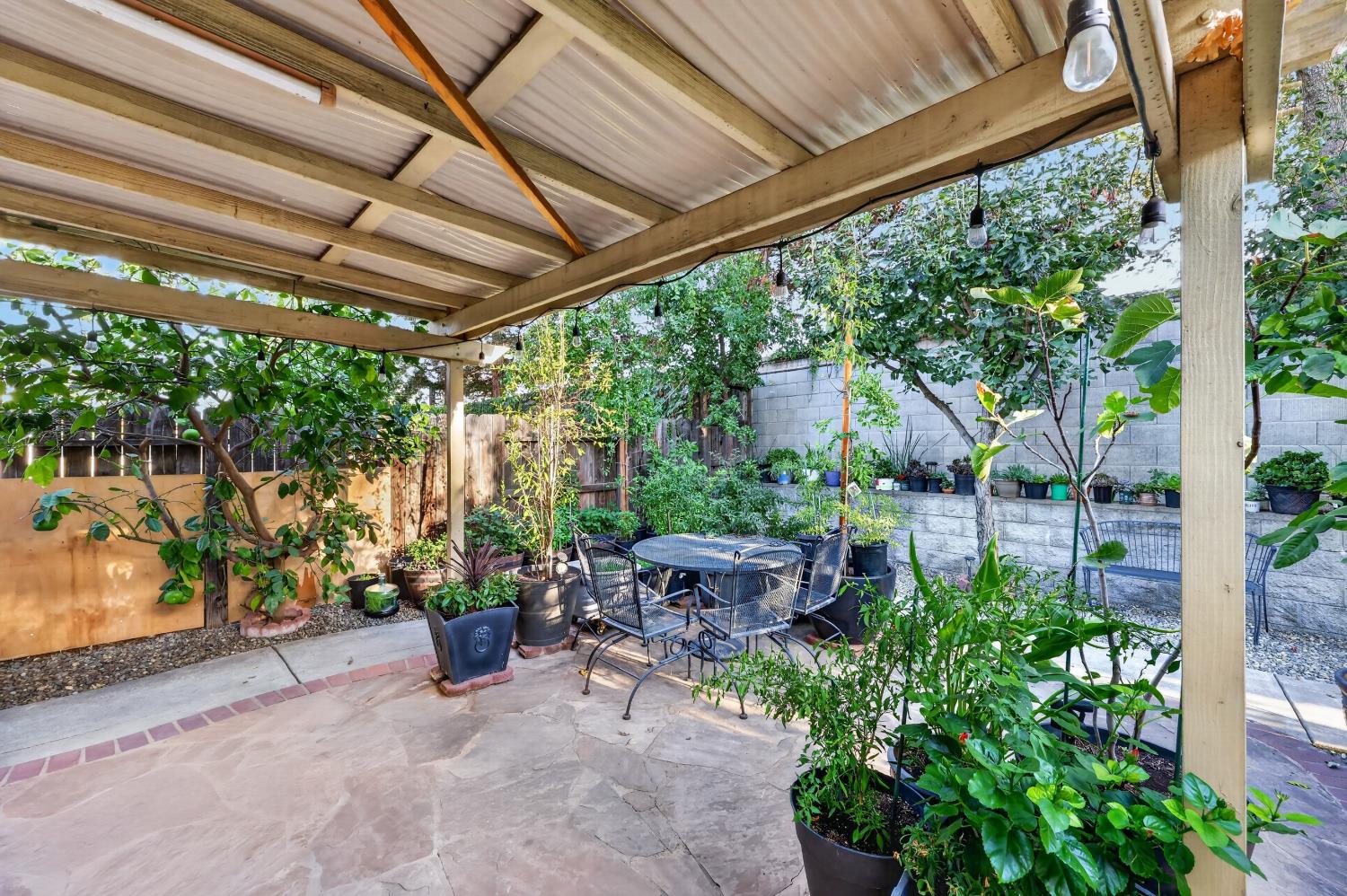 Backyard patio with a pergola, metal dining set, stone paving, and abundant potted plants.
