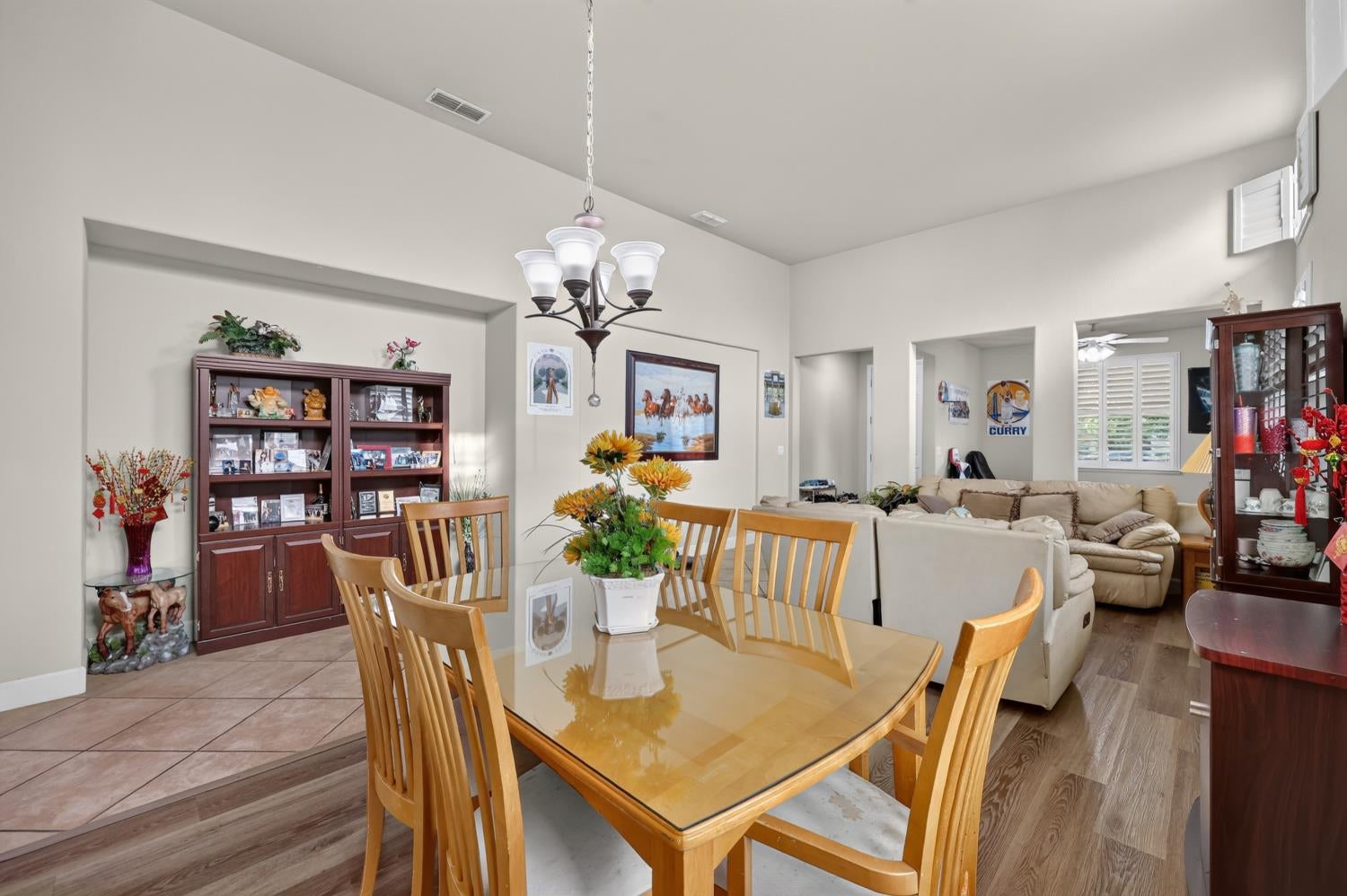 Dining and living area with a glass-top wooden table, beige sectional, and chandelier.