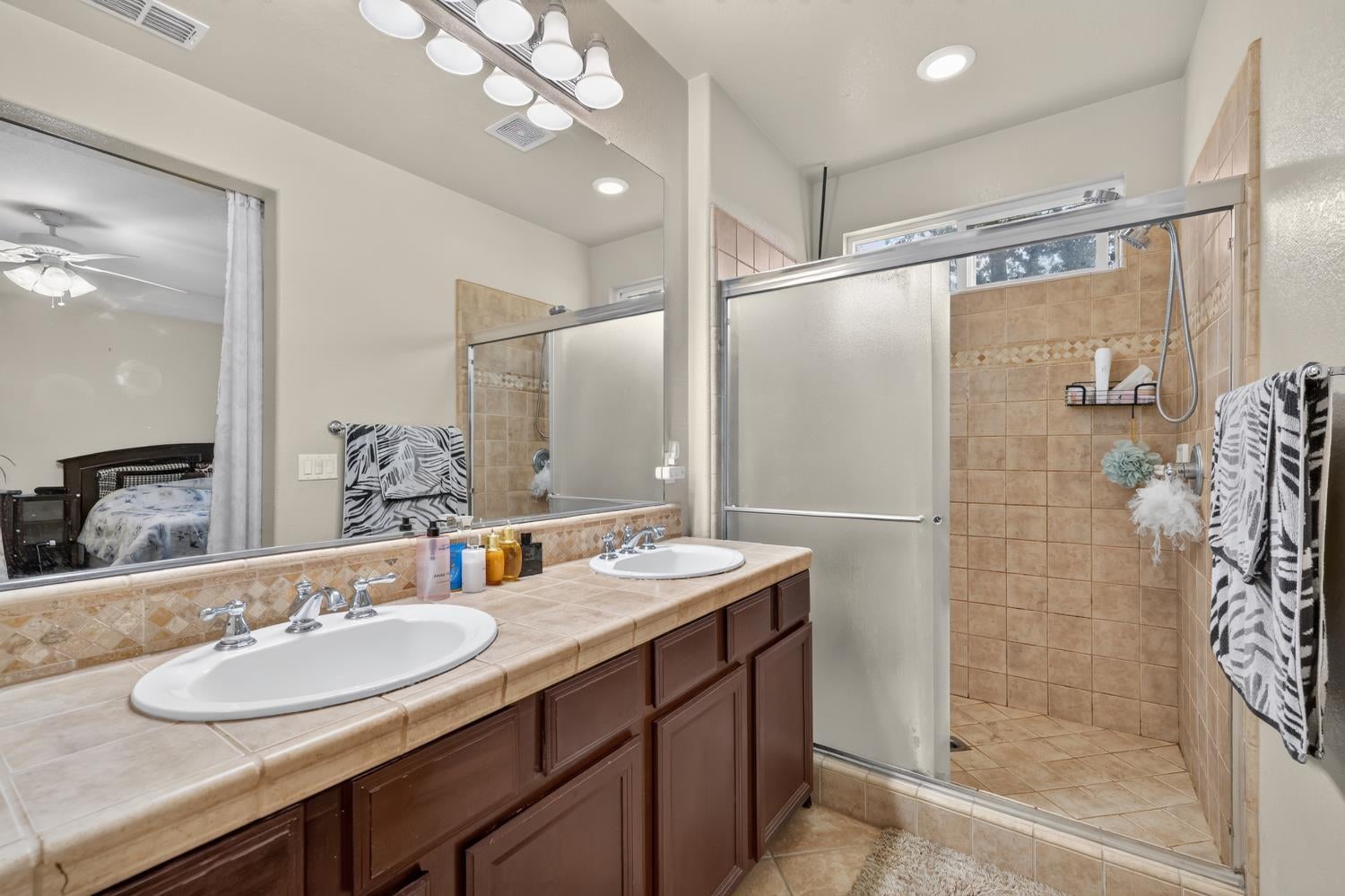 Bathroom with a double-sink vanity, tan tile, and a glass-enclosed shower.