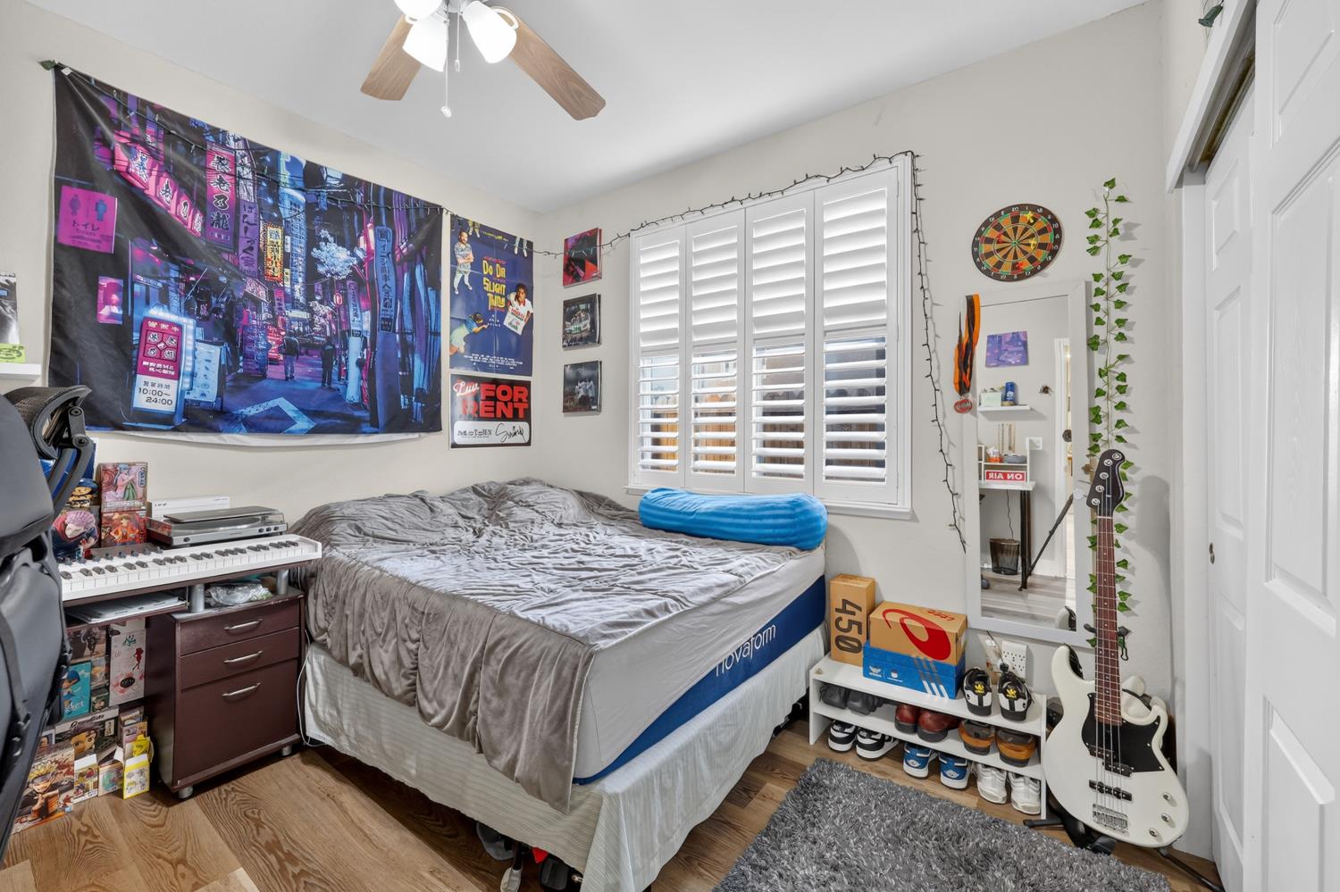 Bedroom with plantation shutters, a keyboard, guitars, and a bed with gray bedding.