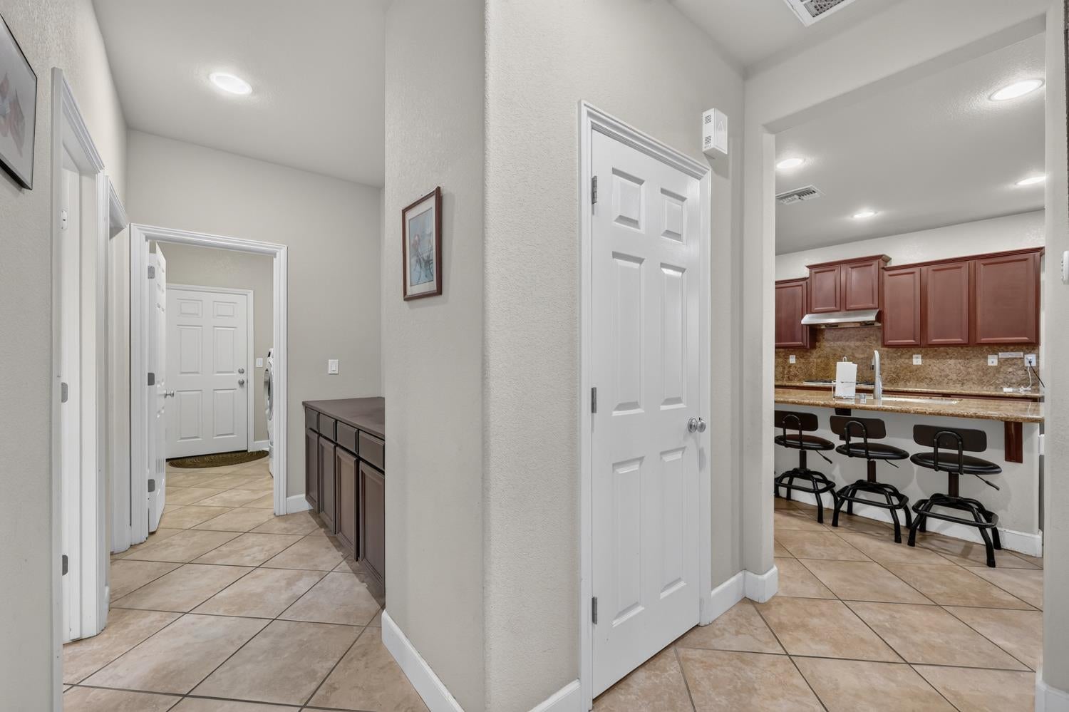 Tiled hallway opening onto a kitchen with a stone counter and three bar stools.