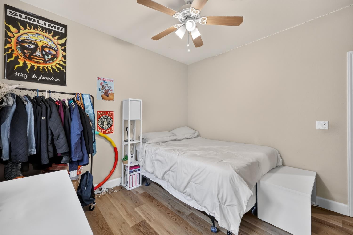 Bedroom with white bedding, a ceiling fan, and a clothing rack beneath wall posters.