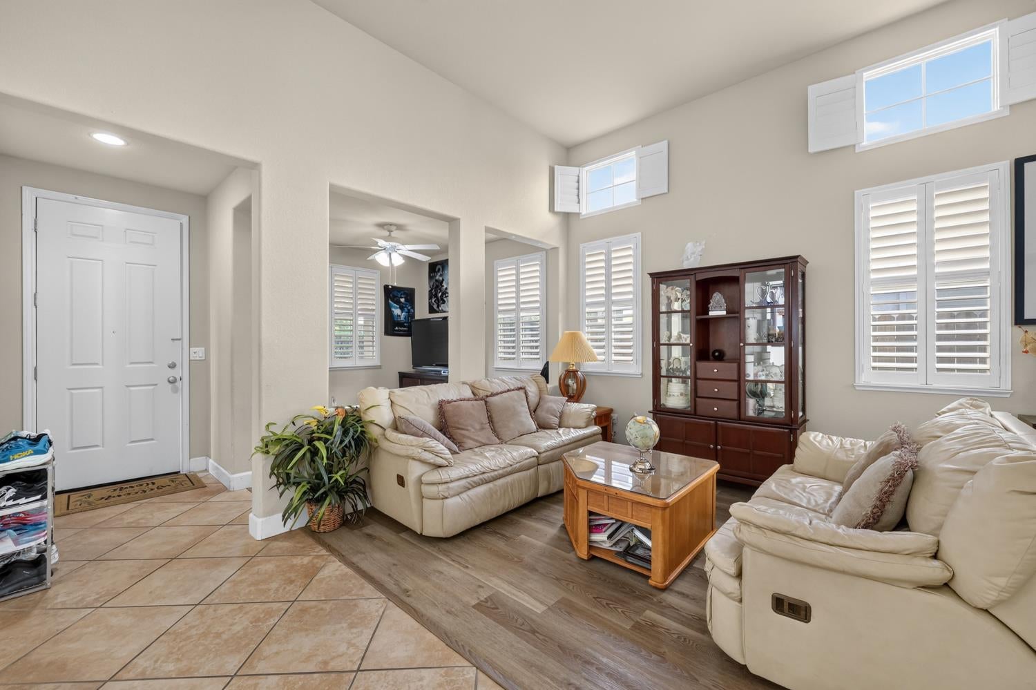 Living room with cream leather sofas, a wooden coffee table, and tall windows with plantation shutters.