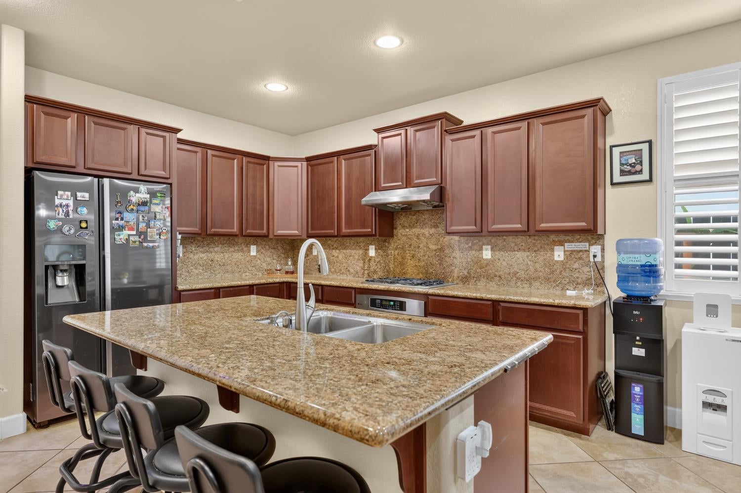 Kitchen with a large granite island, double sink, reddish-brown cabinets, and stainless steel appliances.