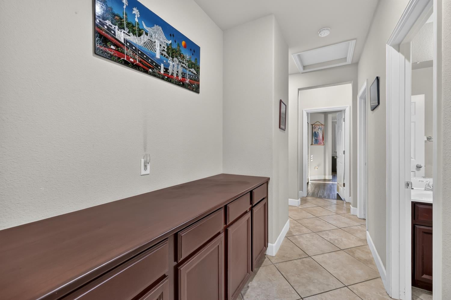 Hallway with dark wood built-in cabinets, beige tile flooring, and colorful artwork.