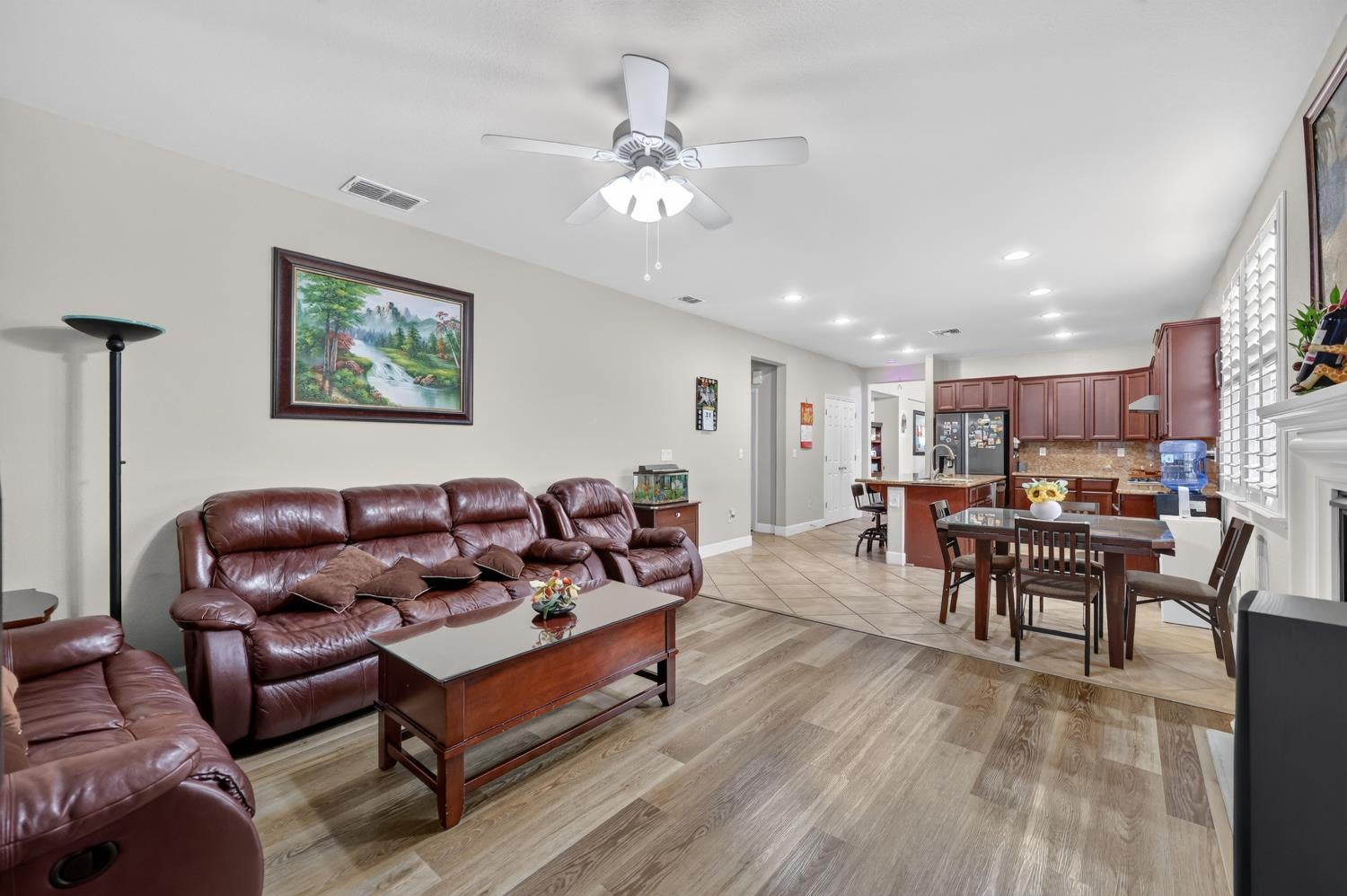 Living room opening to a kitchen, with burgundy leather sofas and wood-look flooring.
