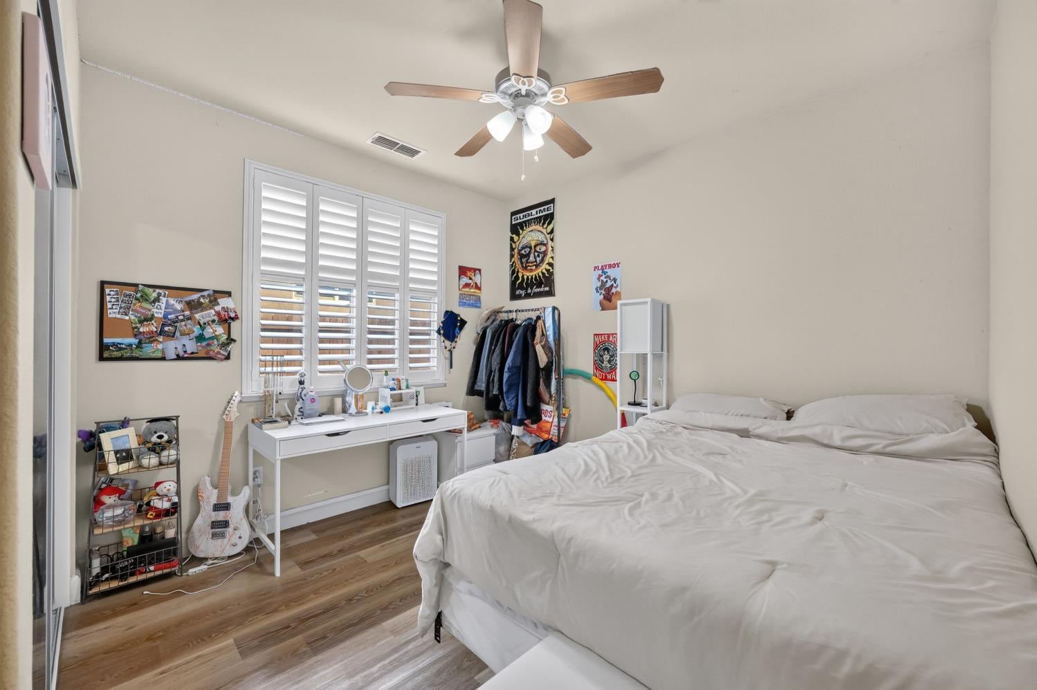 Bedroom with a large white bed, plantation shutters, ceiling fan, and desk.