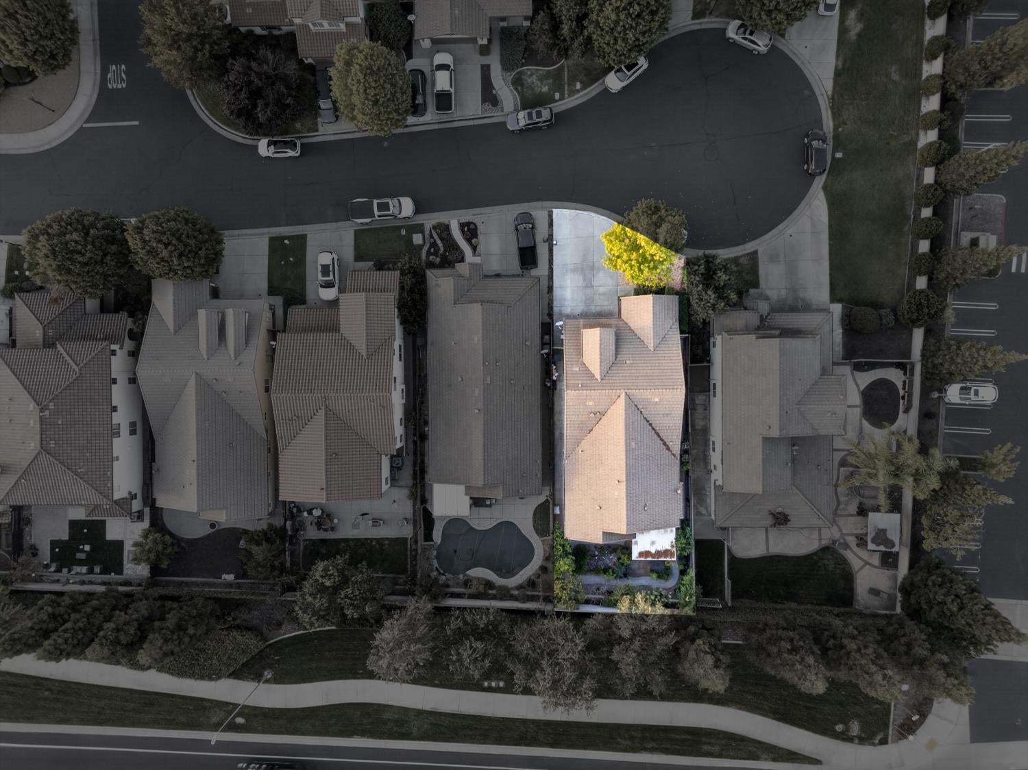 Aerial view of a highlighted tiled-roof home with a backyard pool and landscaped yard.