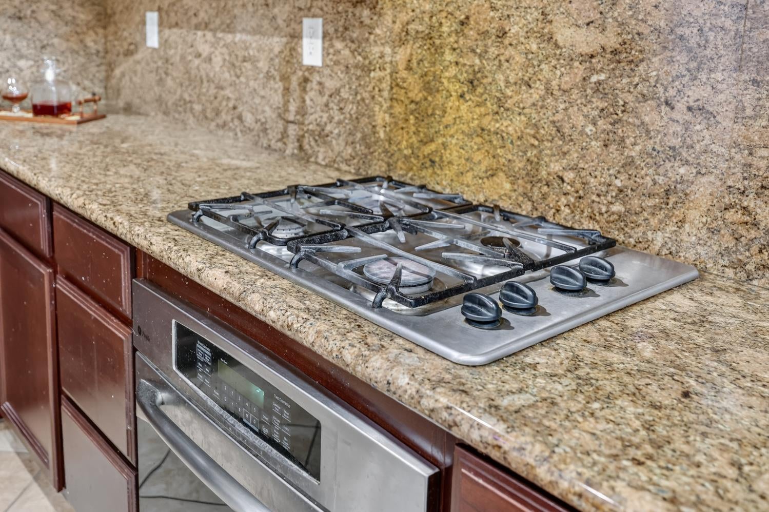 Kitchen gas cooktop and built-in oven set into granite counters and dark wood cabinets.