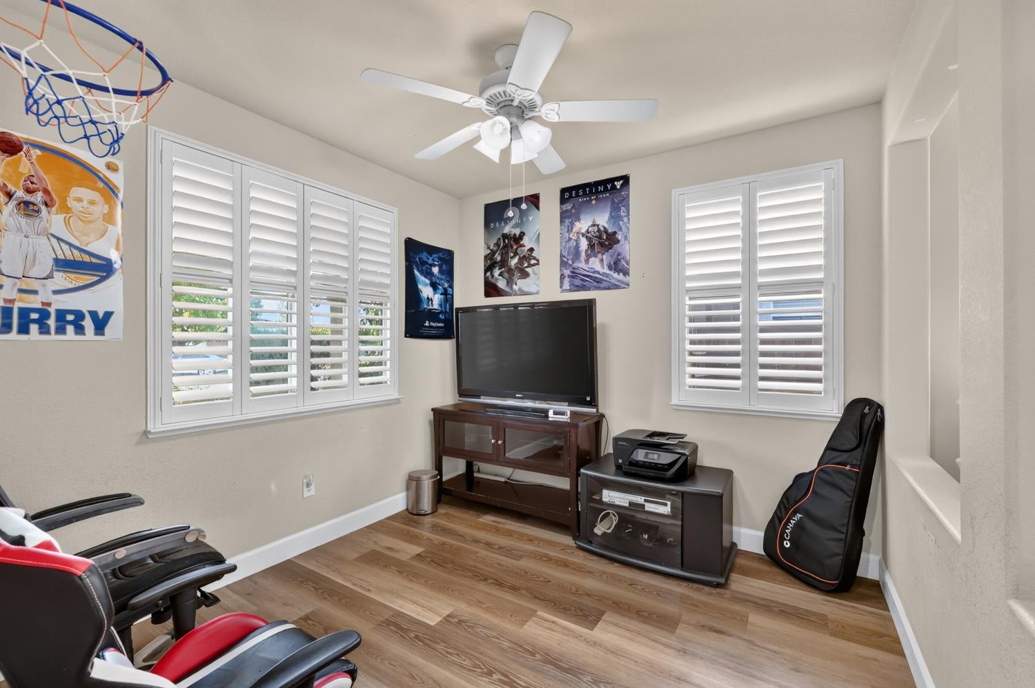 Game room with plantation shutters, a television, gaming posters, and sports memorabilia.