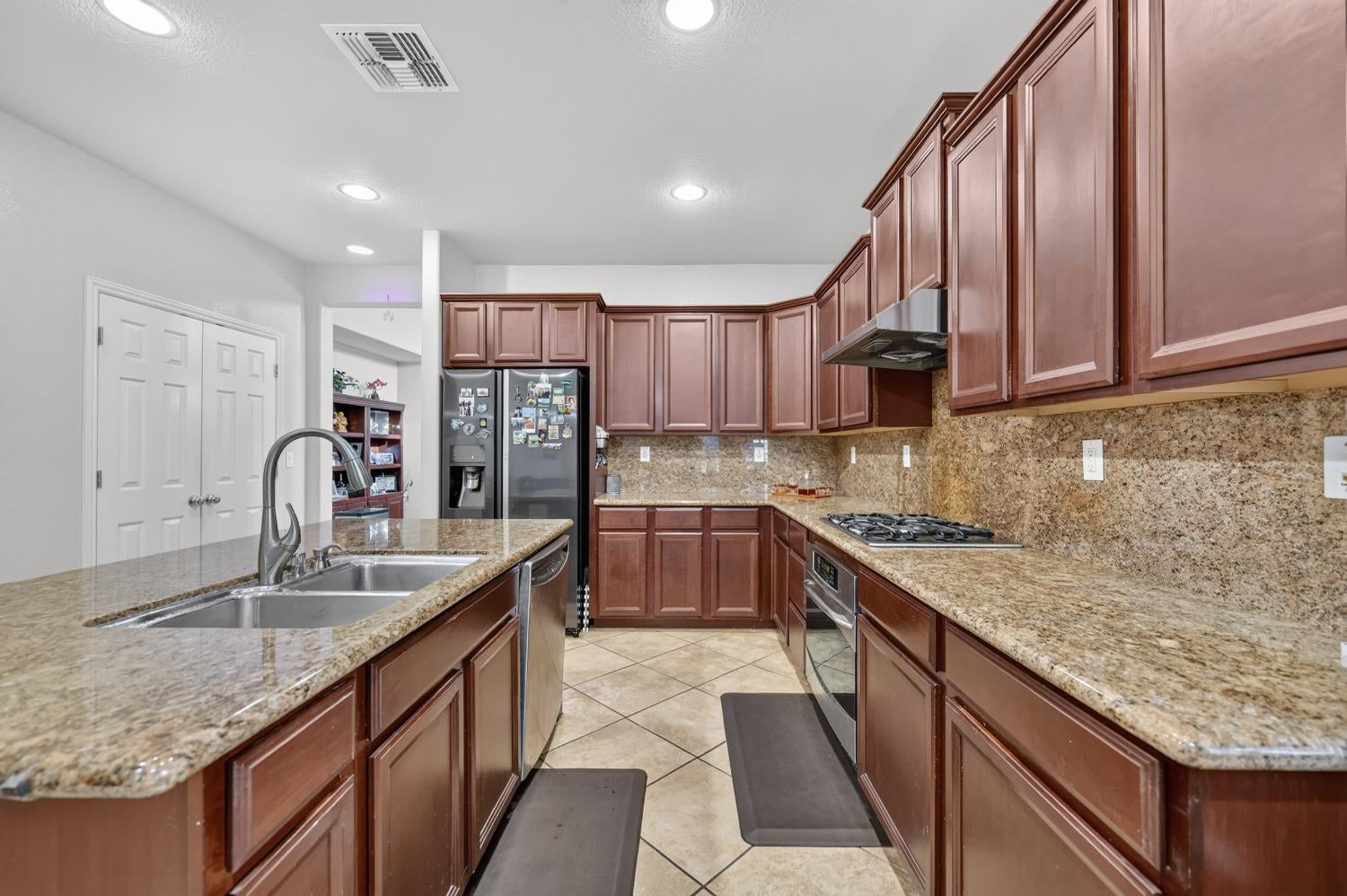 U-shaped kitchen with dark wood cabinets, granite counters, a double sink, and stainless steel appliances.