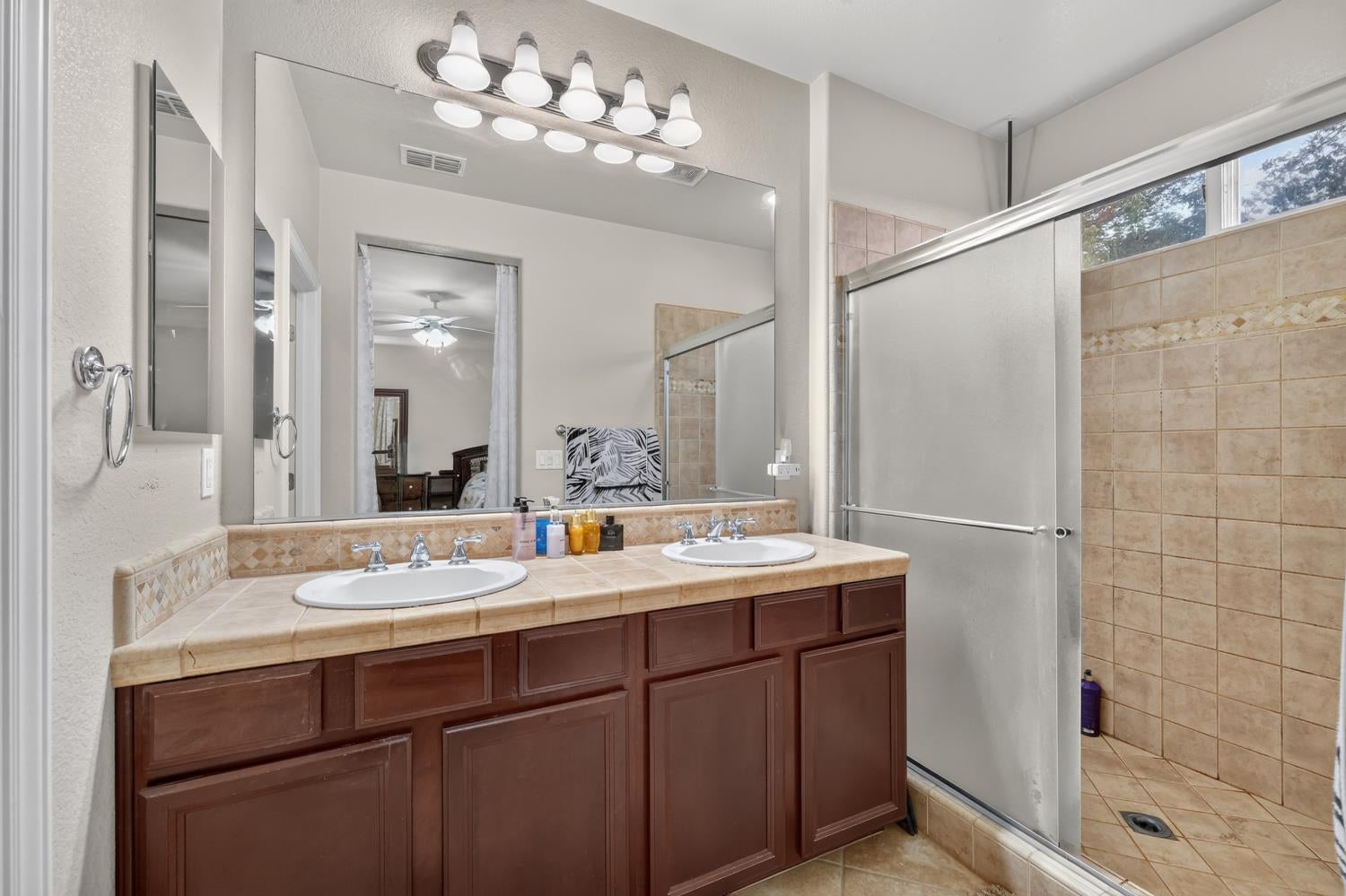 Bathroom with a double-sink vanity, dark wood cabinets, and a tiled glass-enclosed shower.
