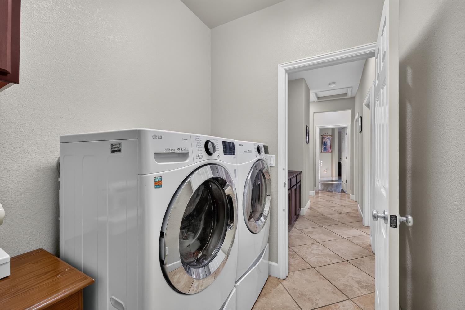 Laundry room with front-loading washer and dryer beside a tiled hallway.