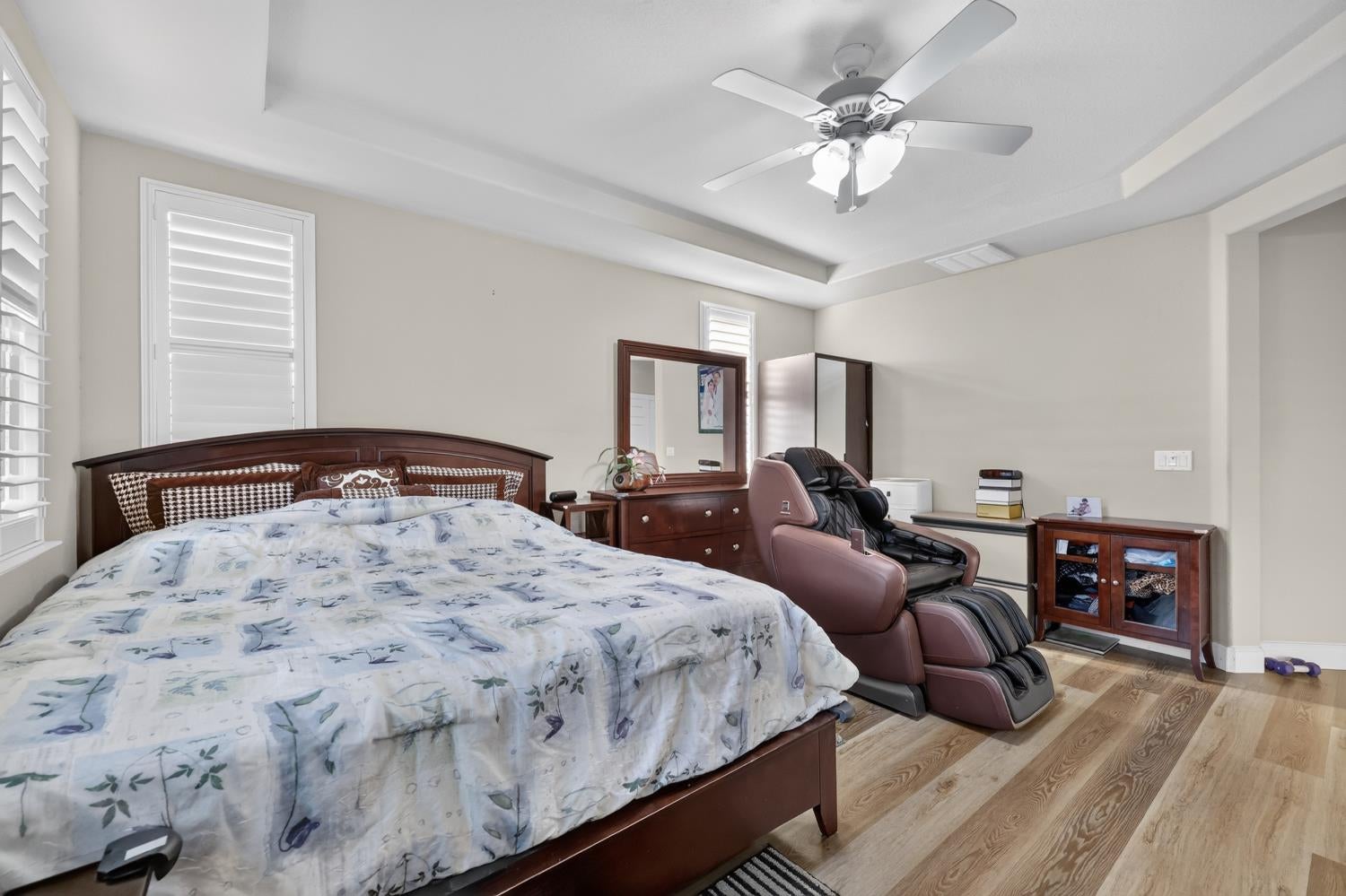 Bedroom with floral bedding, dark wood furnishings, plantation shutters, and a massage chair.