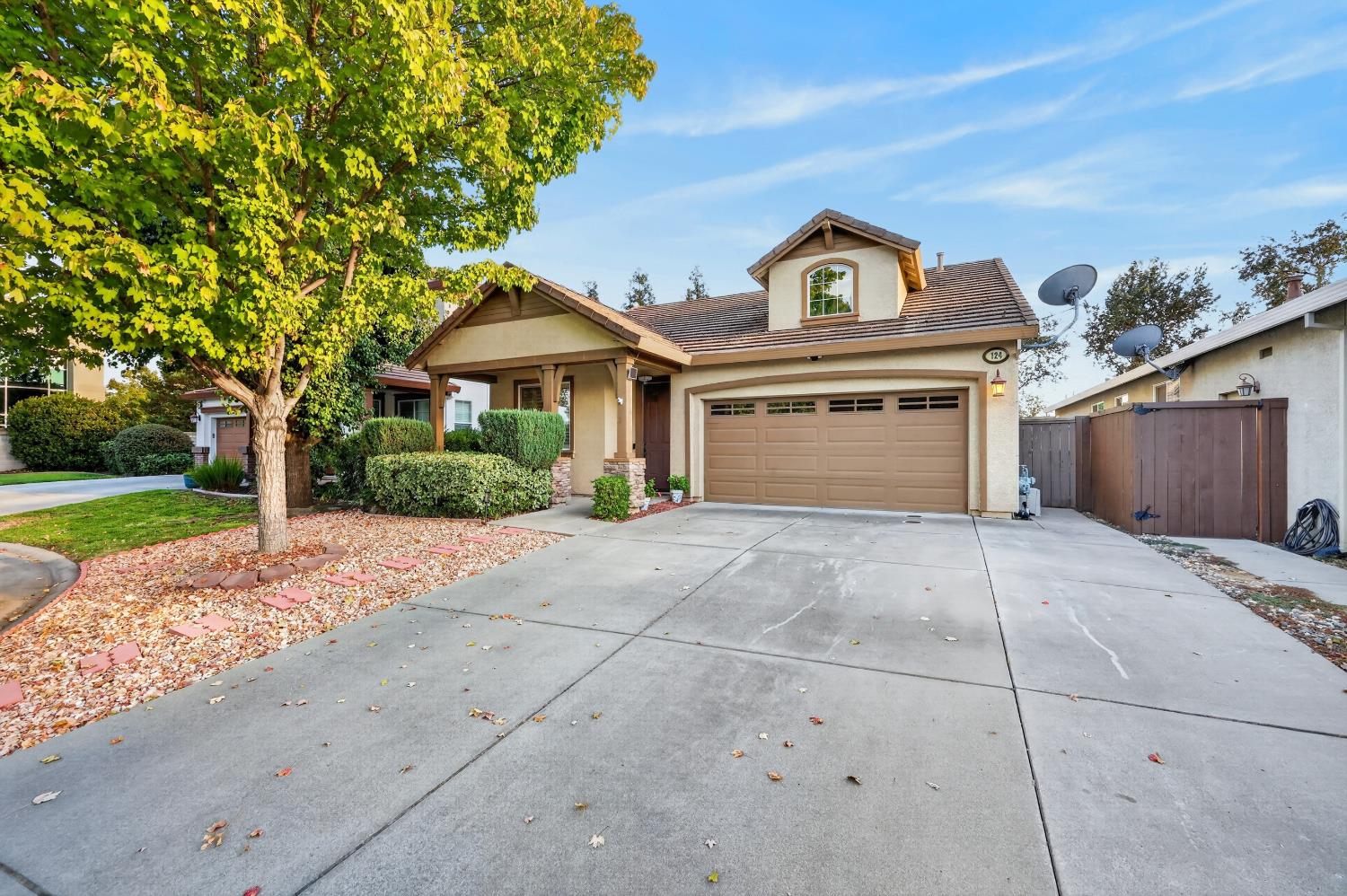Tan stucco home with a covered porch, tile roof, two-car garage, and broad concrete driveway.