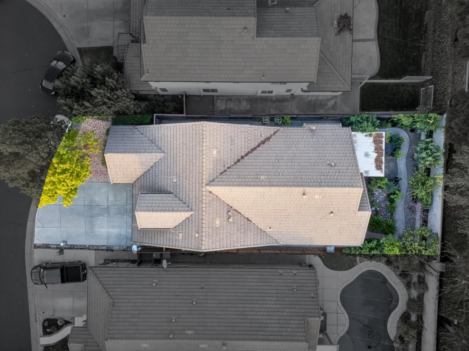 Aerial view of a suburban home with a multi-section tiled roof, driveway, and landscaped yard.