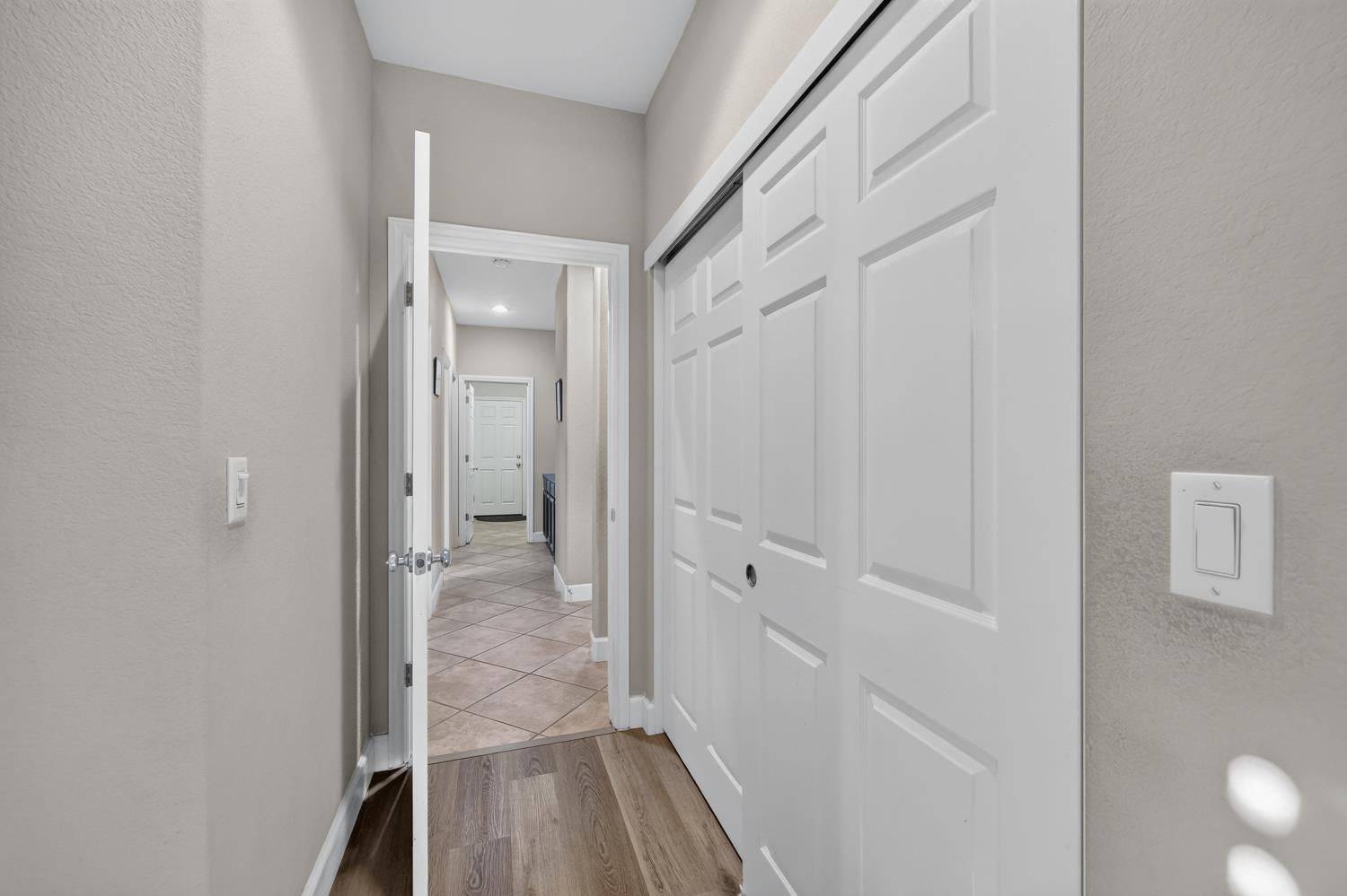 Hallway with white sliding closet doors, wood-look flooring, and a tiled corridor beyond.