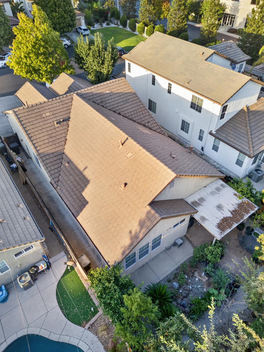 Aerial view of a two-story home with tan tile roofs, landscaped yard, patio, and curved pool.