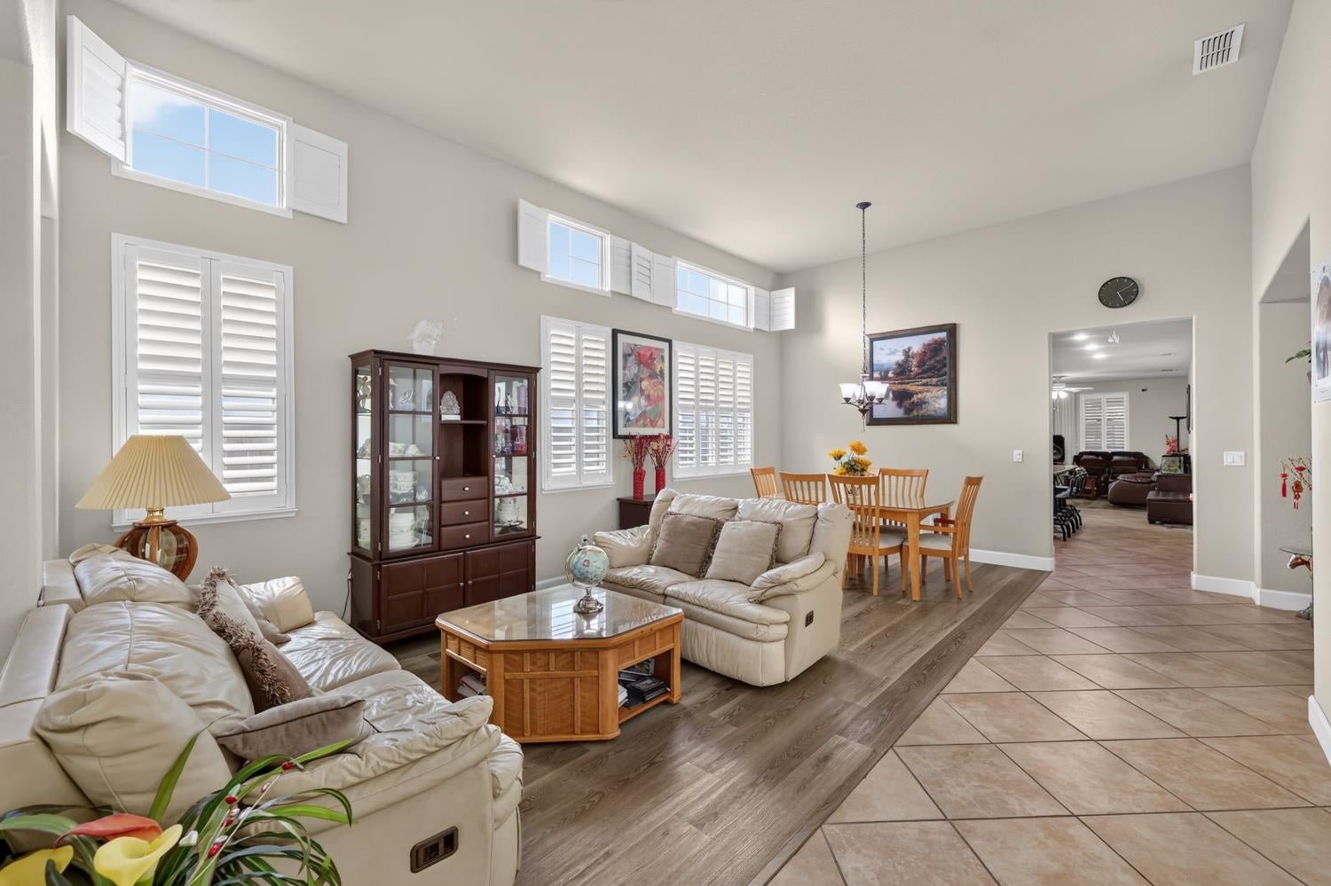 Furnished living room with a vaulted ceiling, plantation shutters, and adjoining dining area.