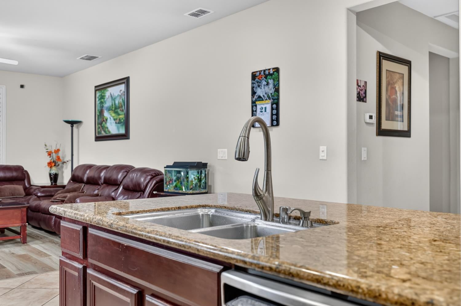 Kitchen island with granite countertop, double-basin sink, and adjoining living area with burgundy leather seating.