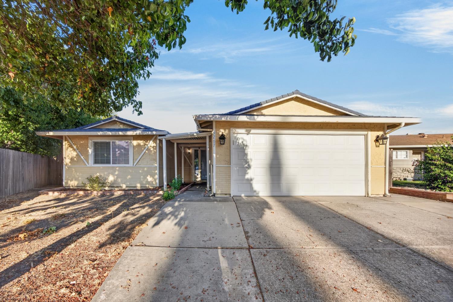 Tan single-story house with a white two-car garage, covered entry, and broad concrete driveway.