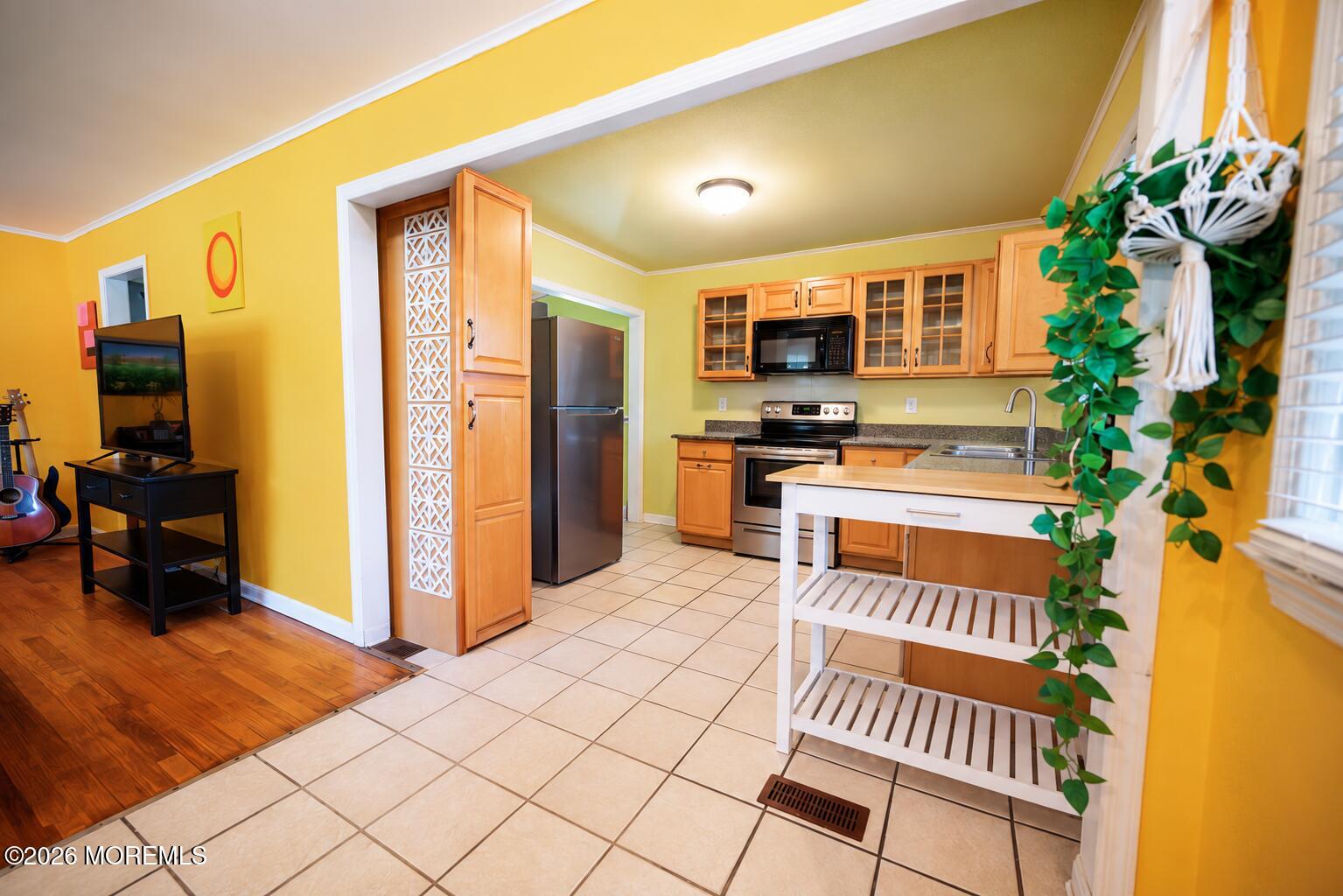 Kitchen with wood cabinets and stainless appliances opening onto a living area with yellow walls.