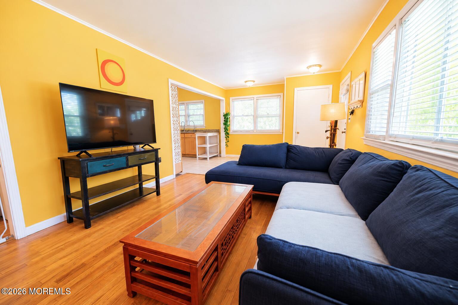 Living room with yellow walls, a navy sectional, hardwood floors, and an opening to the kitchen.