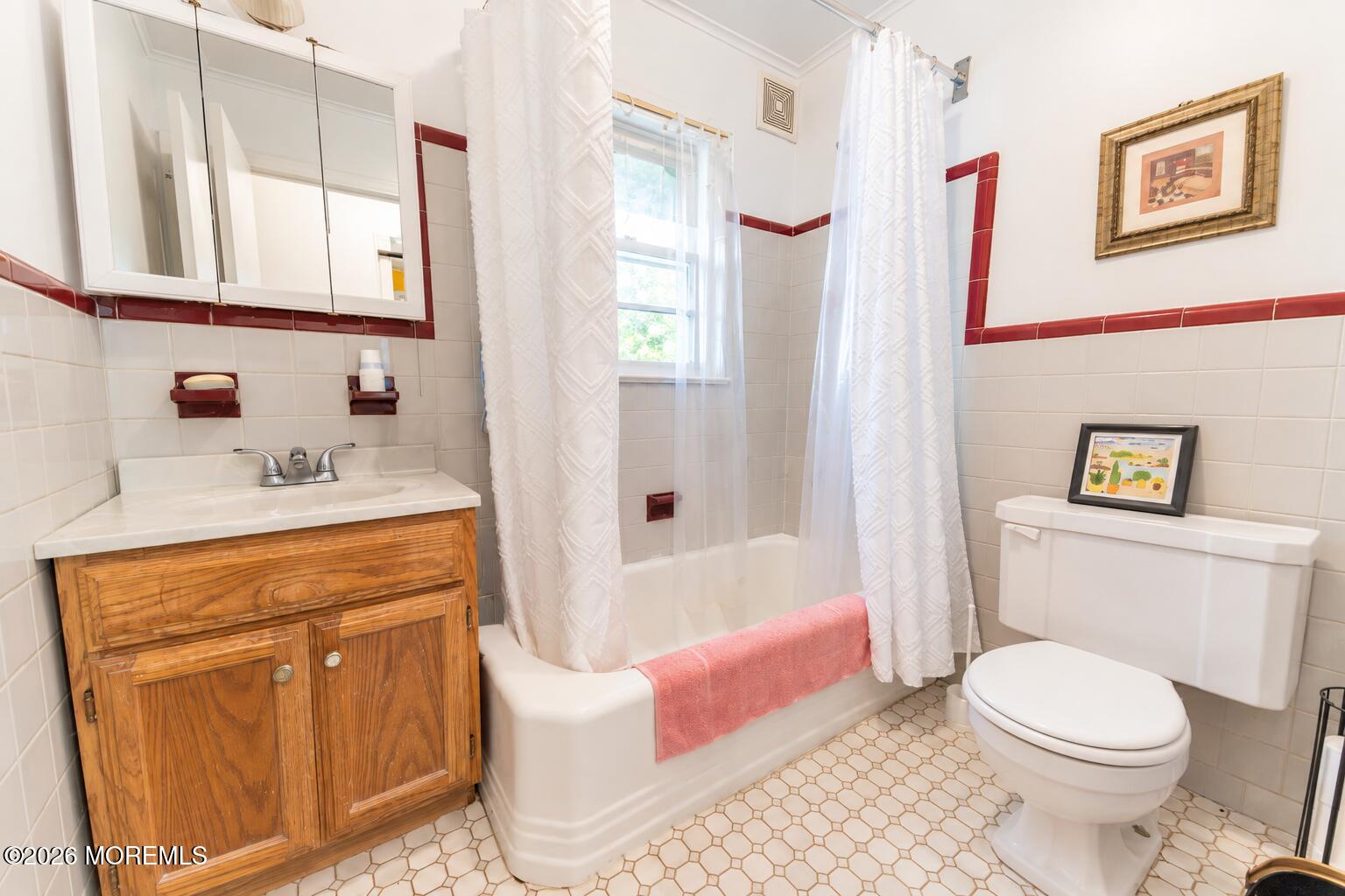 Bathroom with a wooden vanity, white tub, patterned shower curtains, and red tile accents.