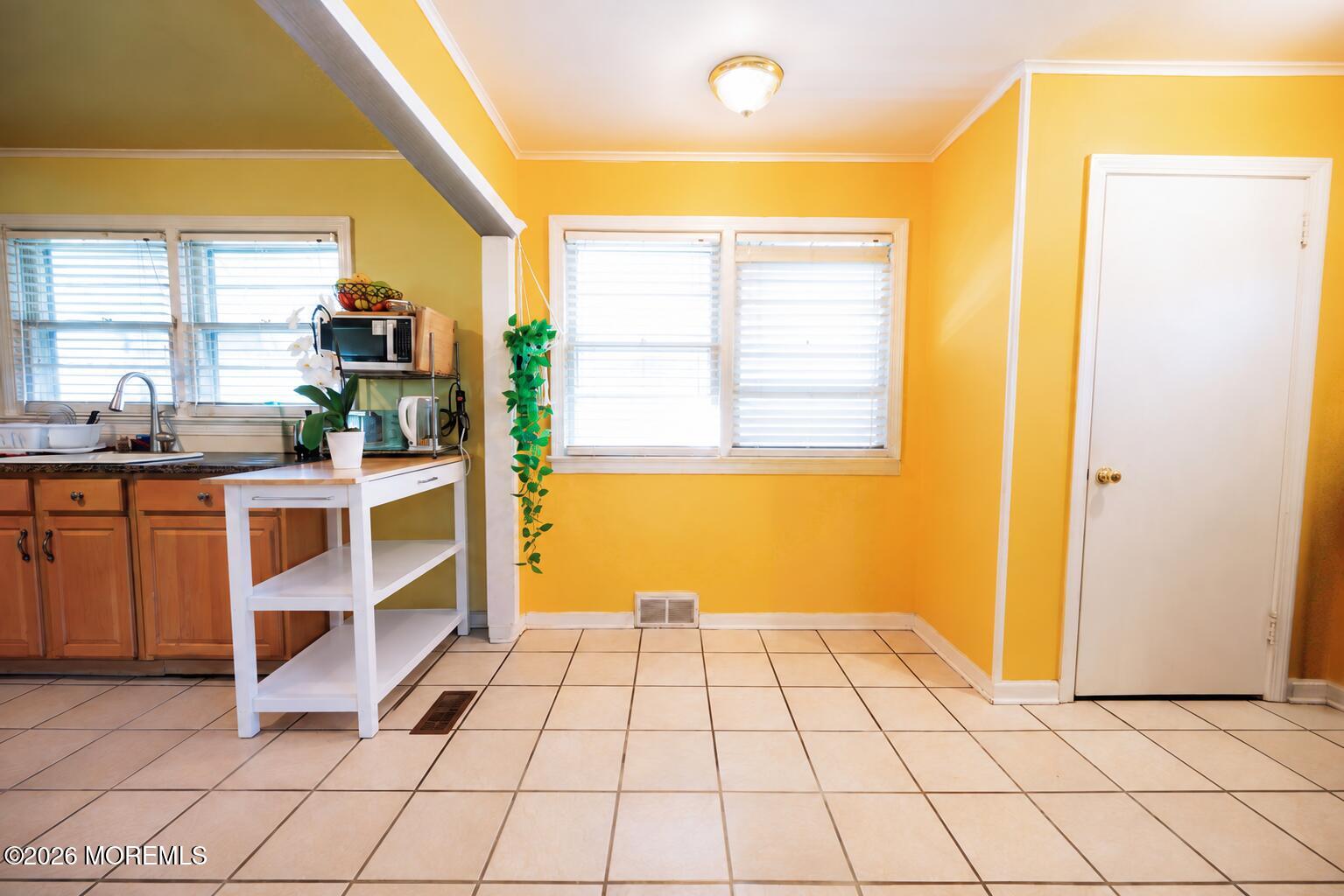 Kitchen with bright yellow walls, tiled floor, wooden cabinets, and a white island cart.