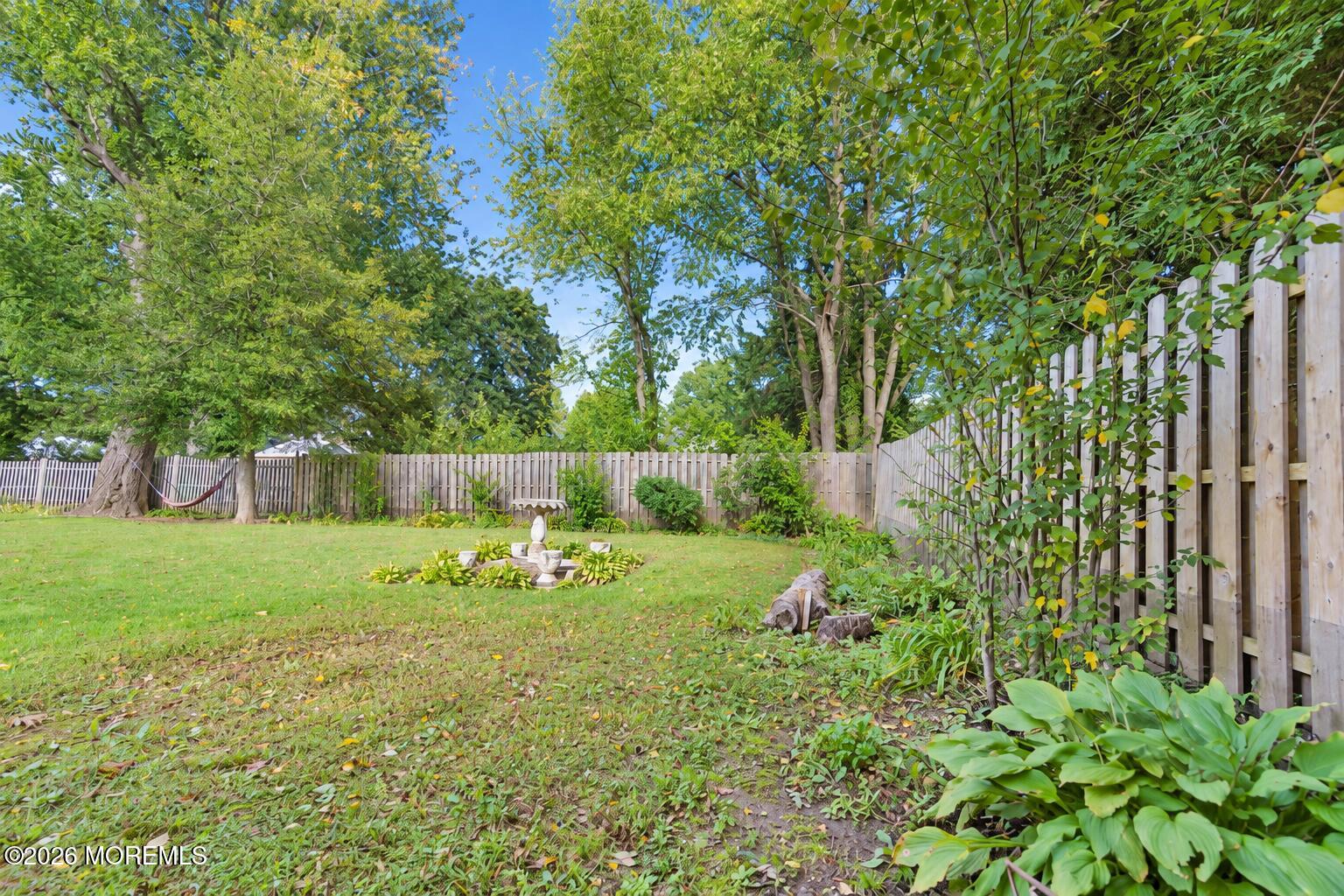 Backyard with a broad lawn, mature trees, wooden fencing, a hammock, and a small fountain.