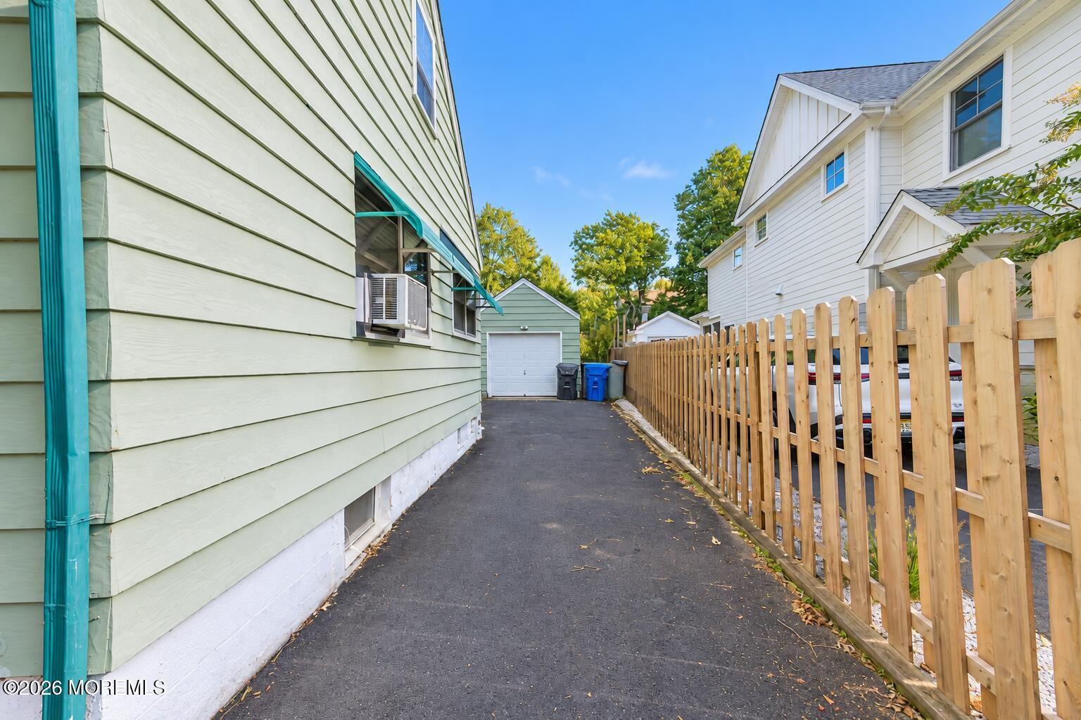 Side driveway leading to a detached garage, bordered by a wooden fence.