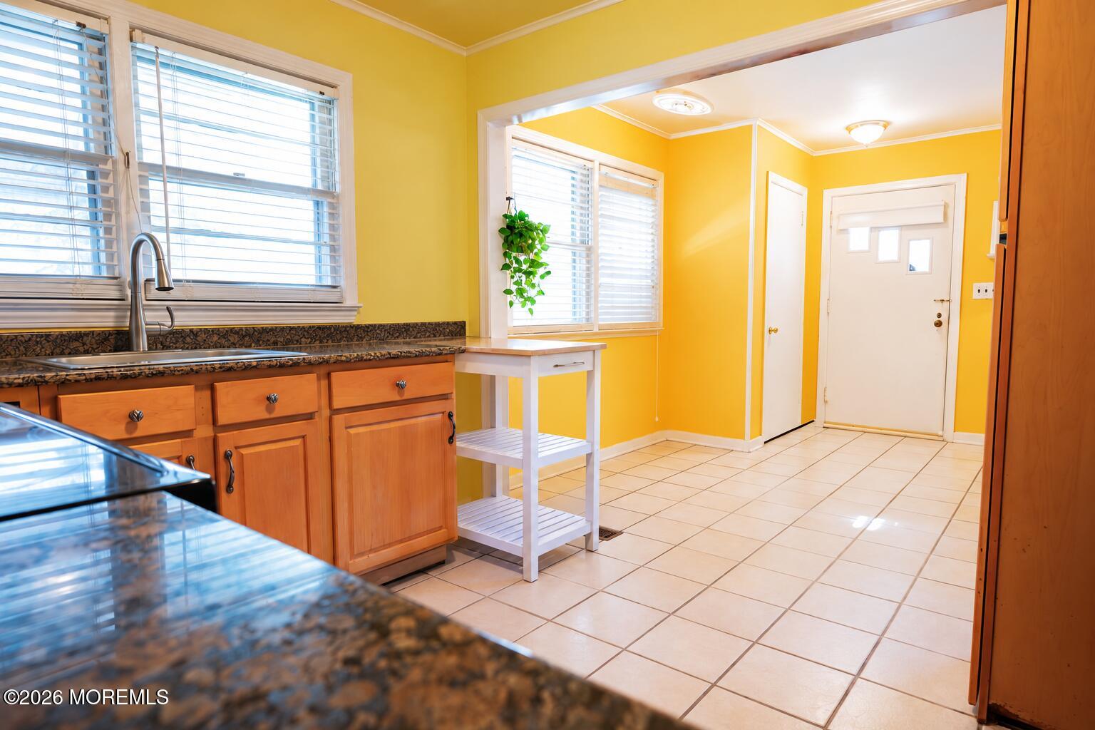 Kitchen with yellow walls, wood cabinets, dark countertops, and a white tile floor.