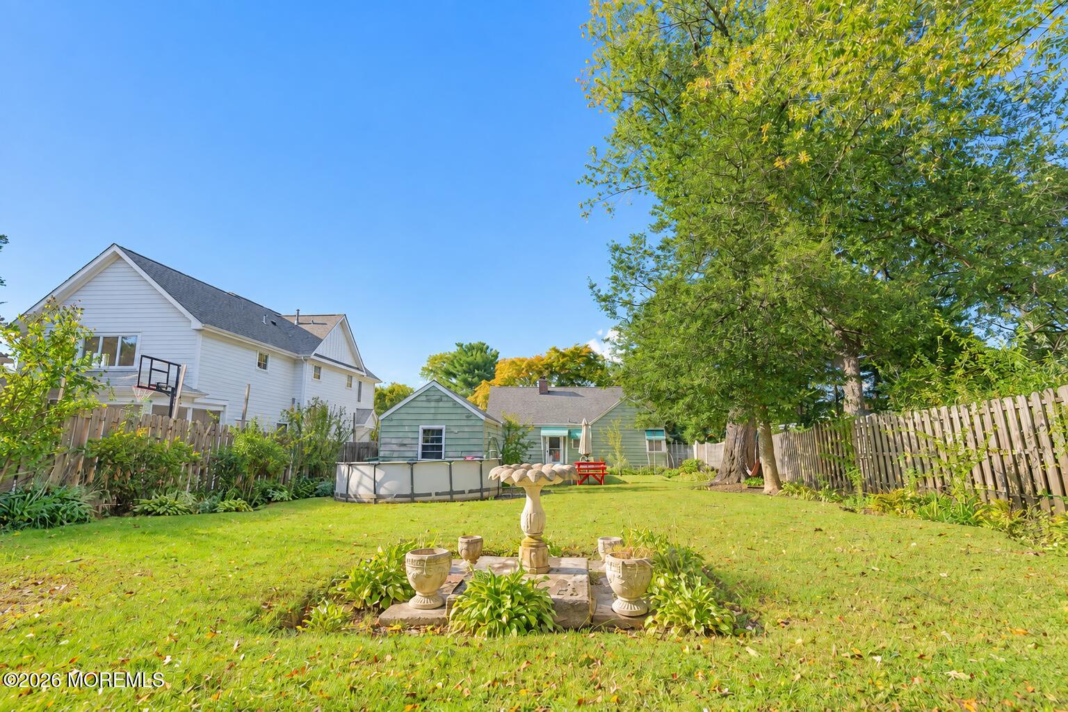 Backyard with a large shade tree, lawn, above-ground pool, and patio ornaments.