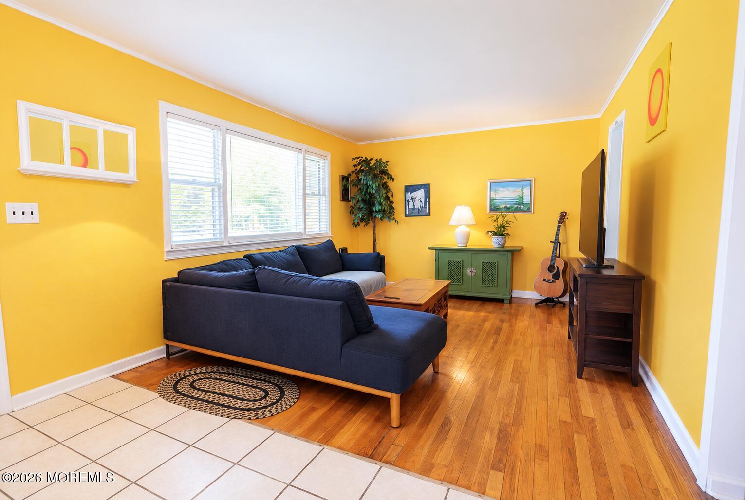 Living room with yellow walls, a navy sectional sofa, hardwood floors, and a wide window with blinds.