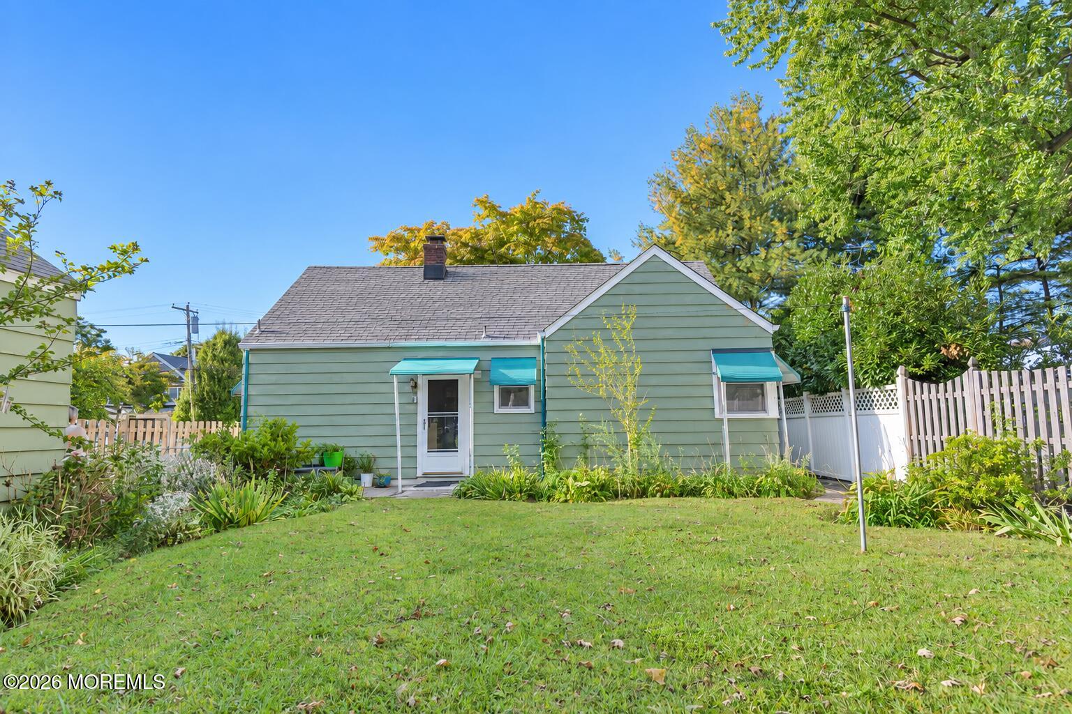 Green-sided house with turquoise awnings, a fenced backyard, and a broad lawn.