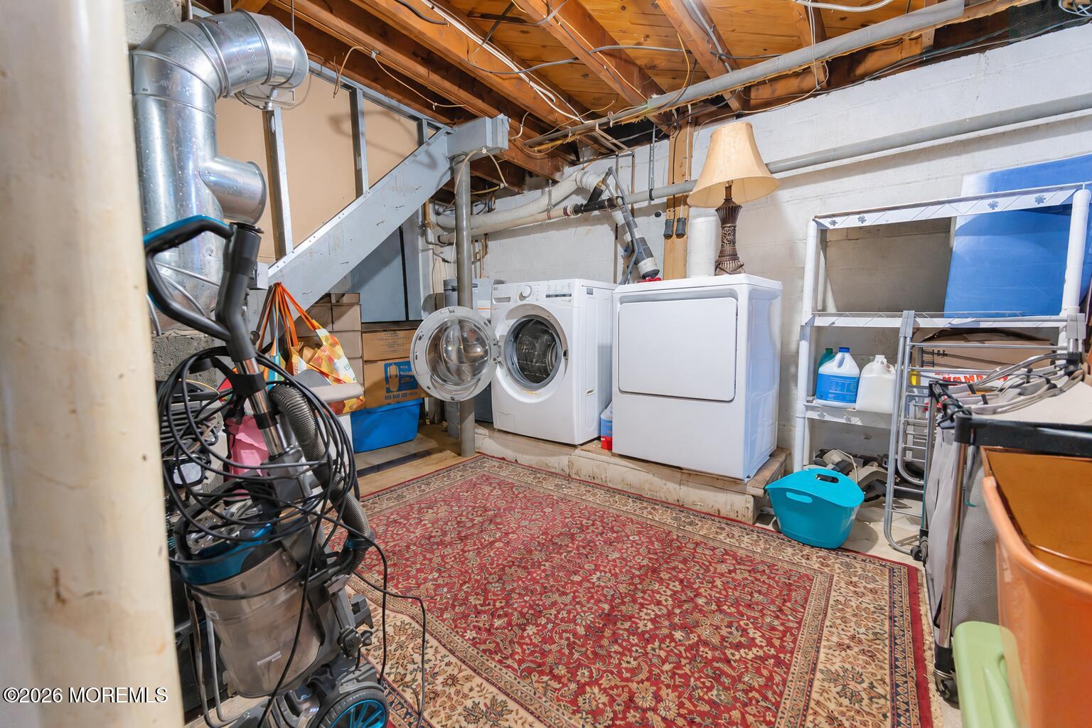 Basement laundry area with a front-loading washer and dryer beneath exposed ceiling joists.
