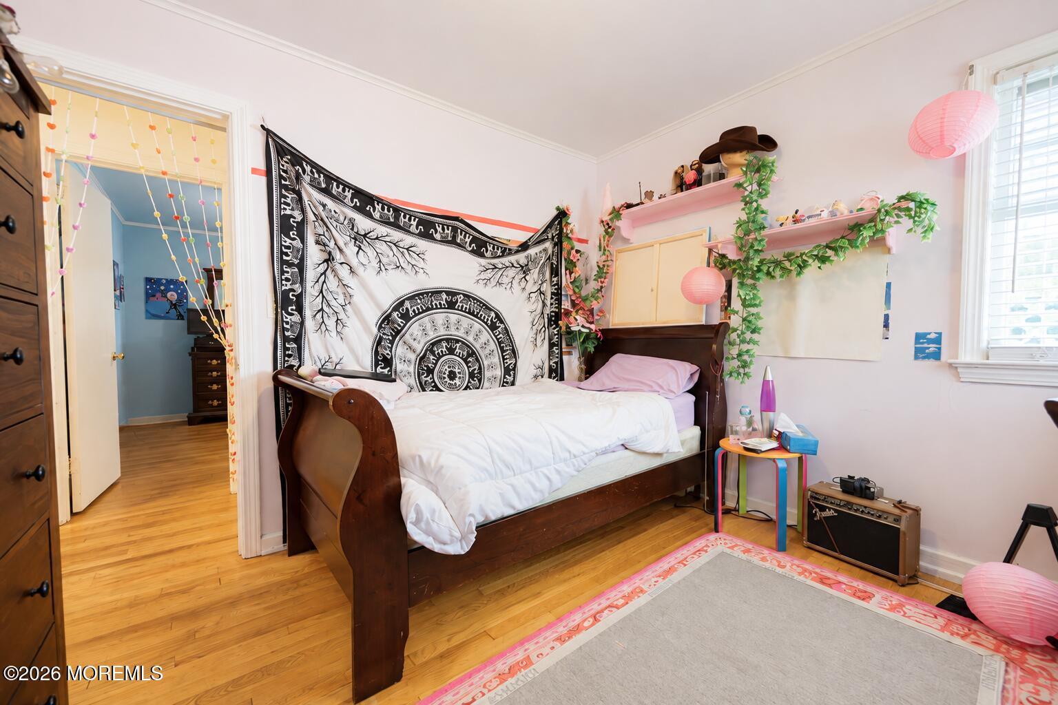 Bedroom with a dark wooden bed, patterned tapestry, pink accents, and hardwood floors.