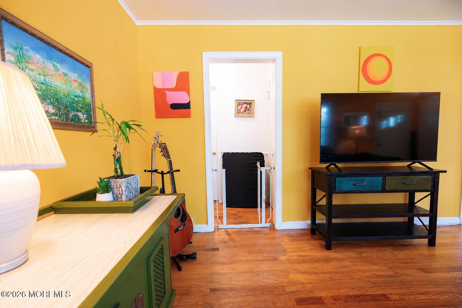 Living room with mustard-yellow walls, hardwood floors, a television, and a guitar beside a green desk.
