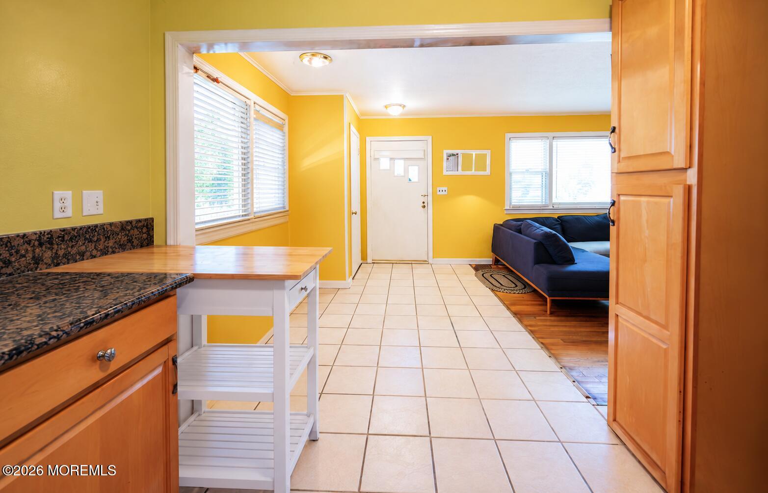 Kitchen with yellow walls, granite counters, and a view into a living room with a blue sectional.