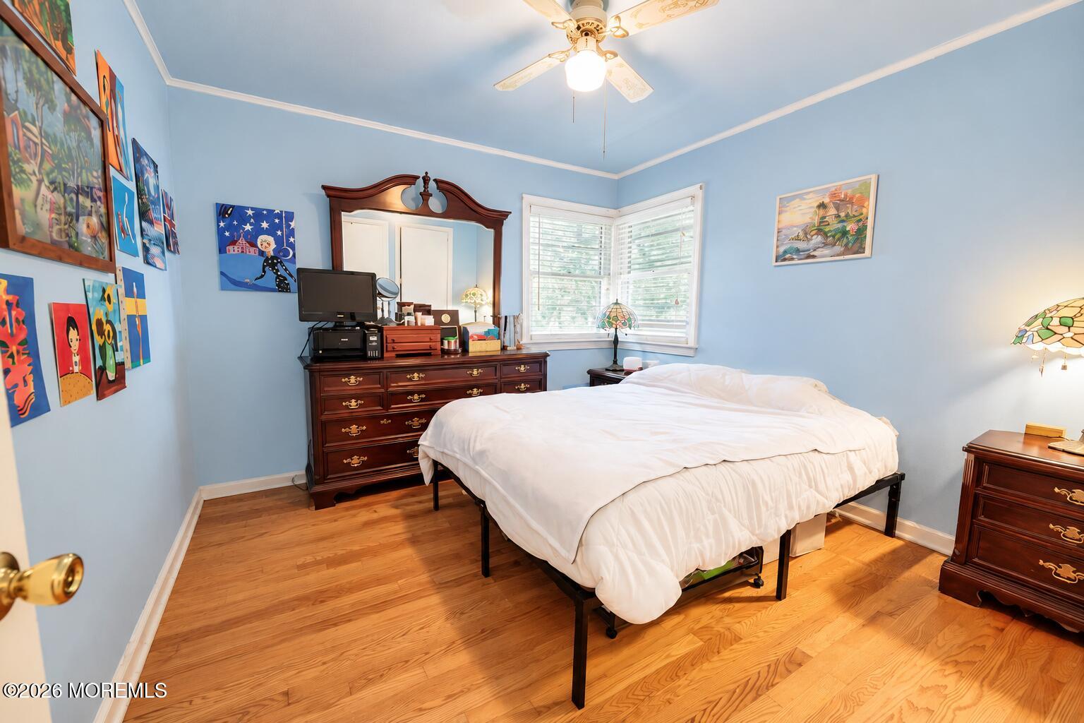 Bedroom with pale blue walls, hardwood floors, a white bed, and colorful wall art.