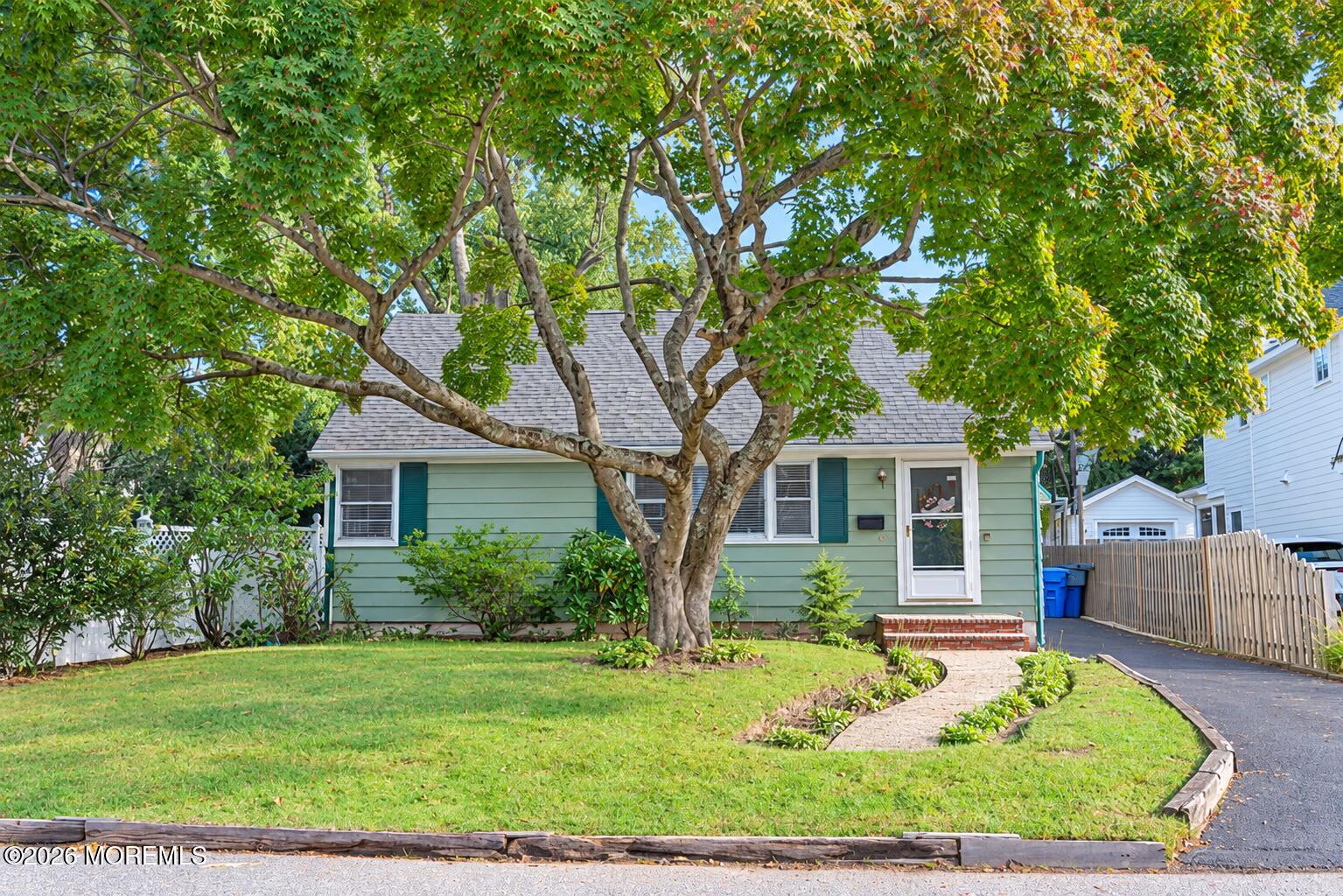 Pale green single-story home with teal shutters, shaded by a large tree and fronted by a curved walkway.