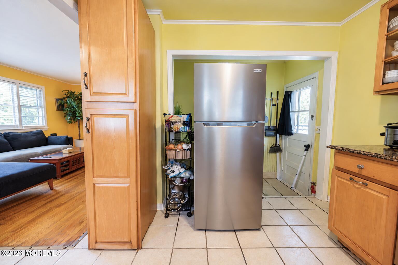 Kitchen with stainless steel refrigerator and light wood cabinets opening to a living room.