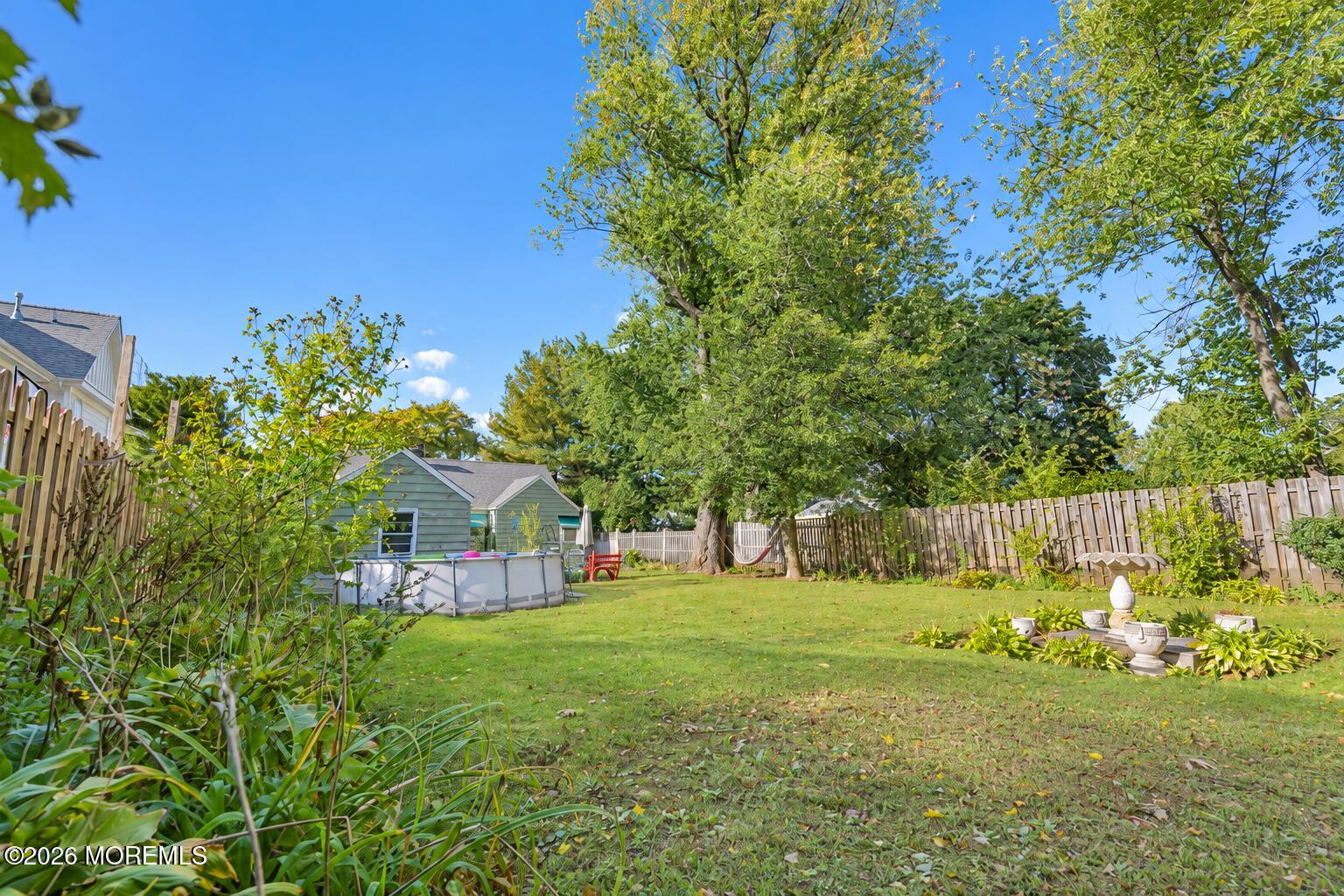 Backyard with an above-ground pool, mature trees, lawn, and wooden fencing.