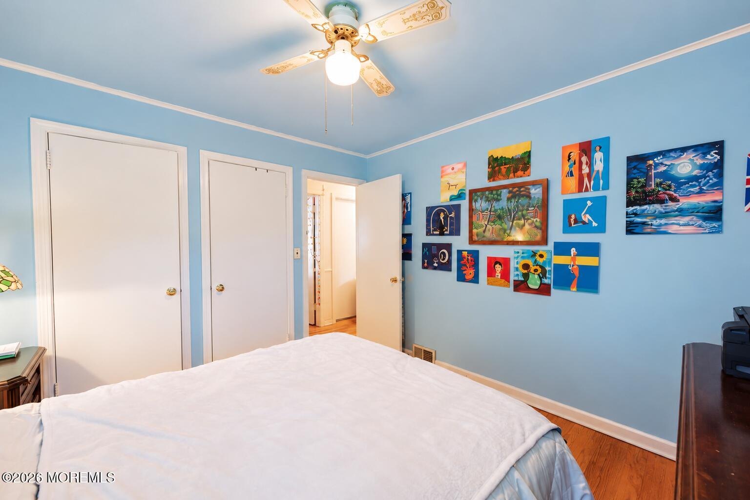 Bedroom with blue walls, a white bed, colorful wall art, and a decorative ceiling fan.