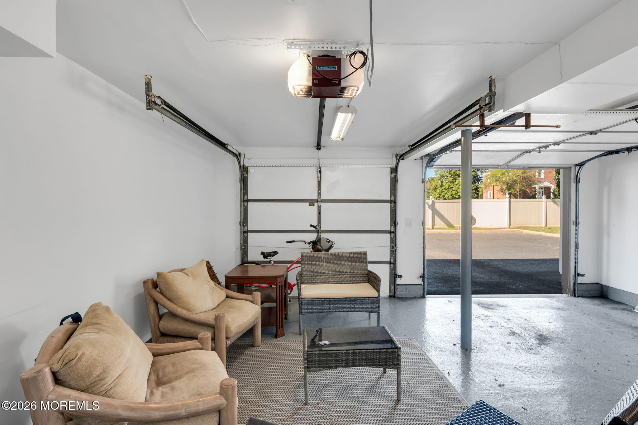 Garage seating area with cushioned chairs and wicker loveseat beside an open garage door.