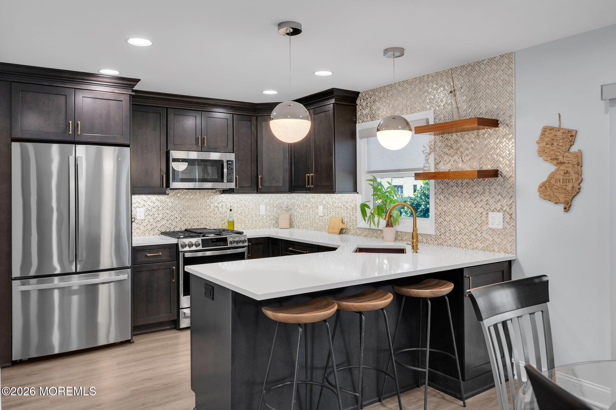 Kitchen with dark cabinets, stainless steel appliances, patterned tile backsplash, and a white island with stools.